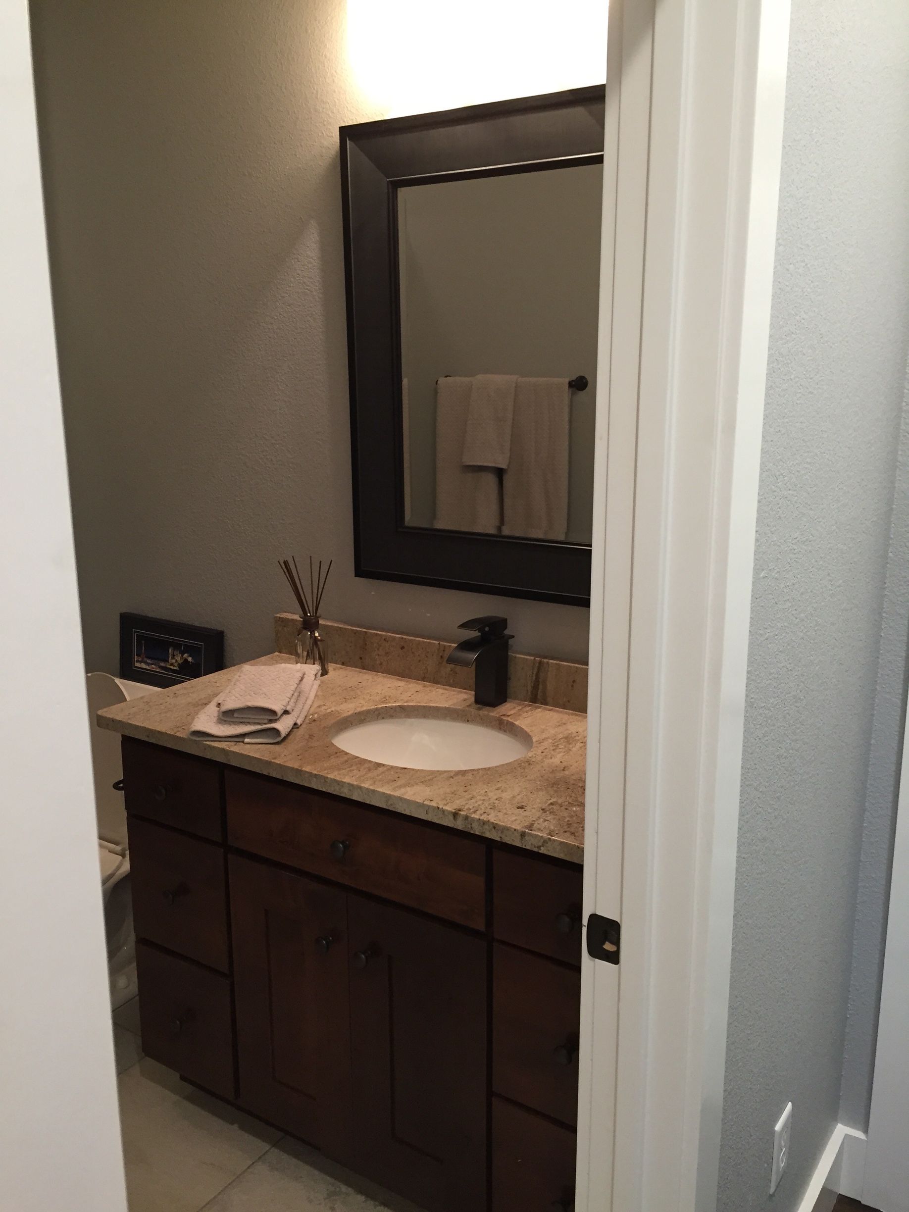 Small bathroom vanity with granite countertop, mirror, sink, and dark wood cabinets.