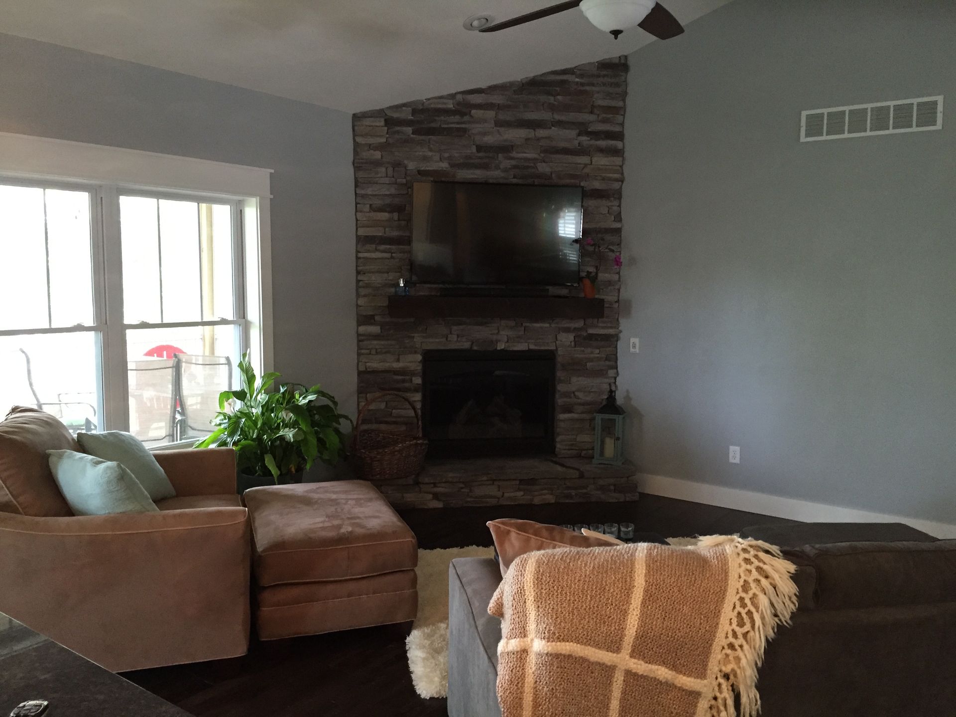 Cozy living room with brown sectional, stone fireplace, wall-mounted TV, and a plant by the window