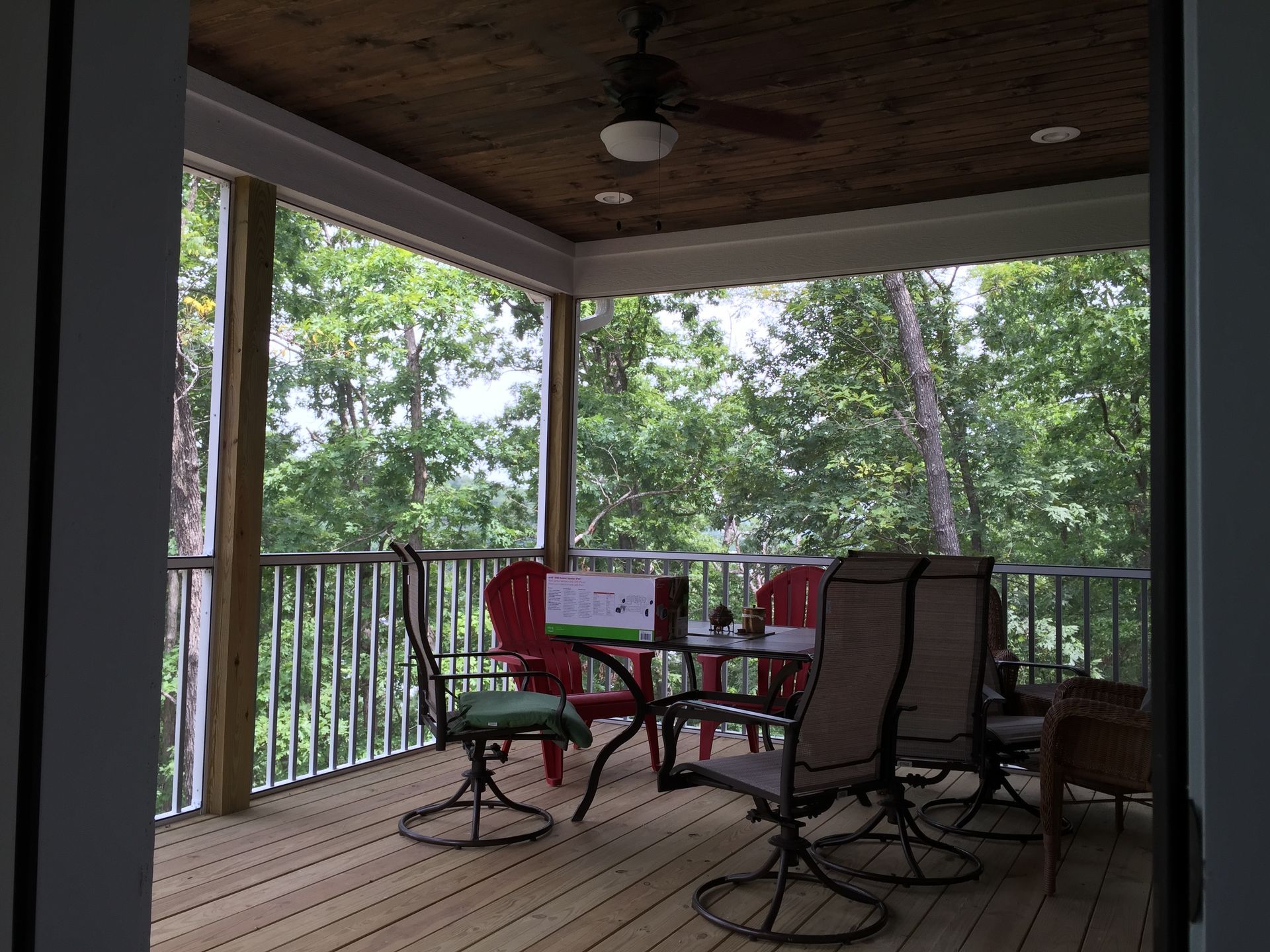 Covered porch with red chairs and a glass table overlooking trees and greenery