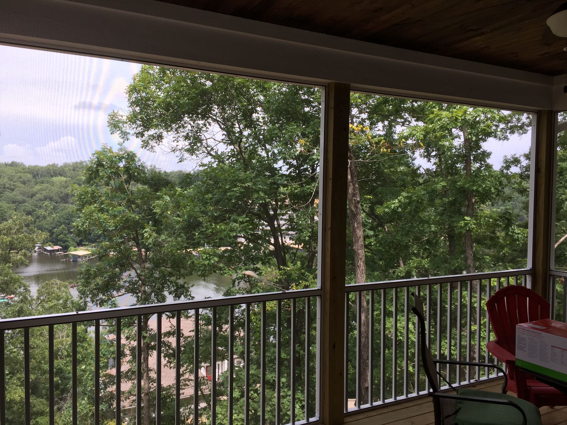 Covered porch overlooking leafy trees and a calm lake, with railing and a red chair in the foreground