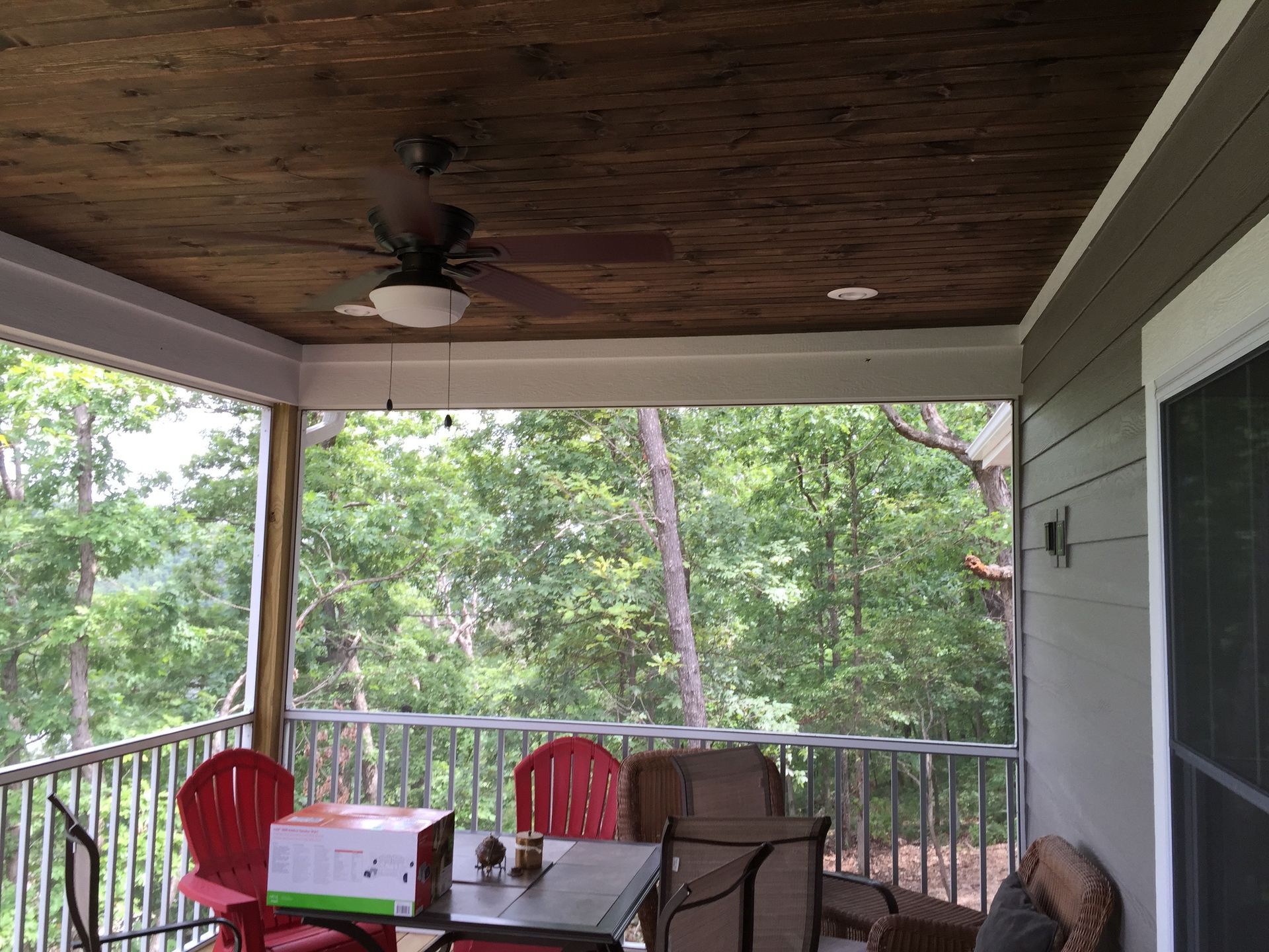 Covered porch with red chairs and a white cooler overlooking a wooded backyard
