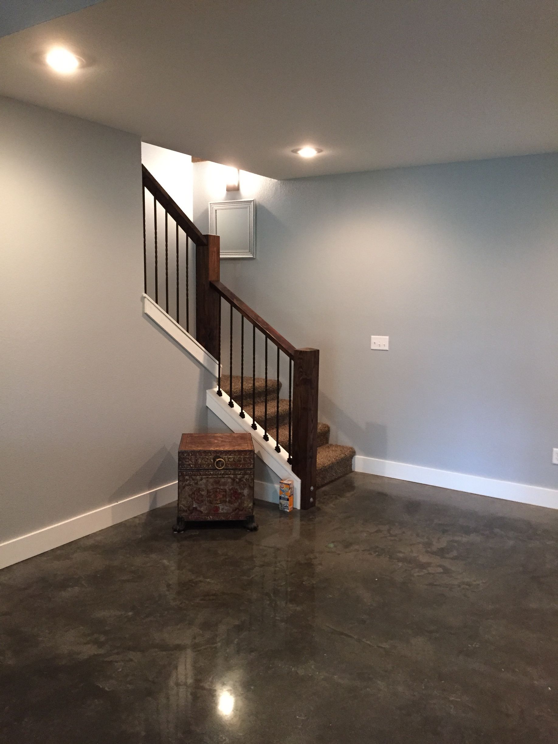 Empty finished basement with gray walls, dark floor, staircase, and a small storage cabinet.