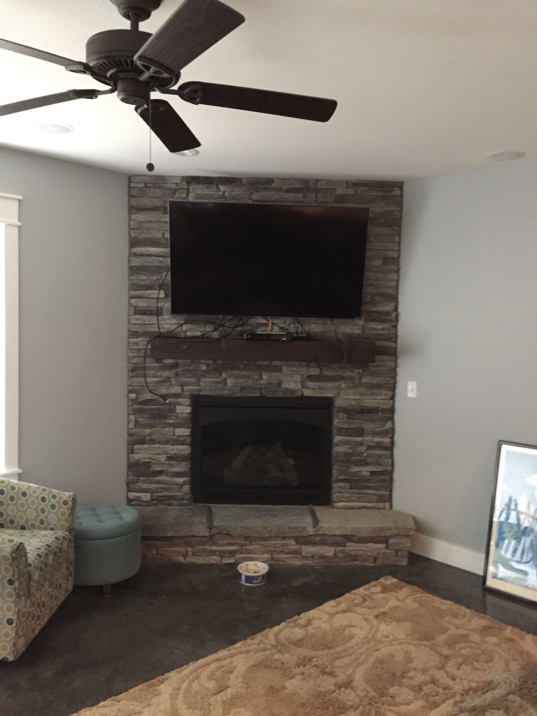 Living room with mounted TV above a stone fireplace, ceiling fan, couch, and beige rug