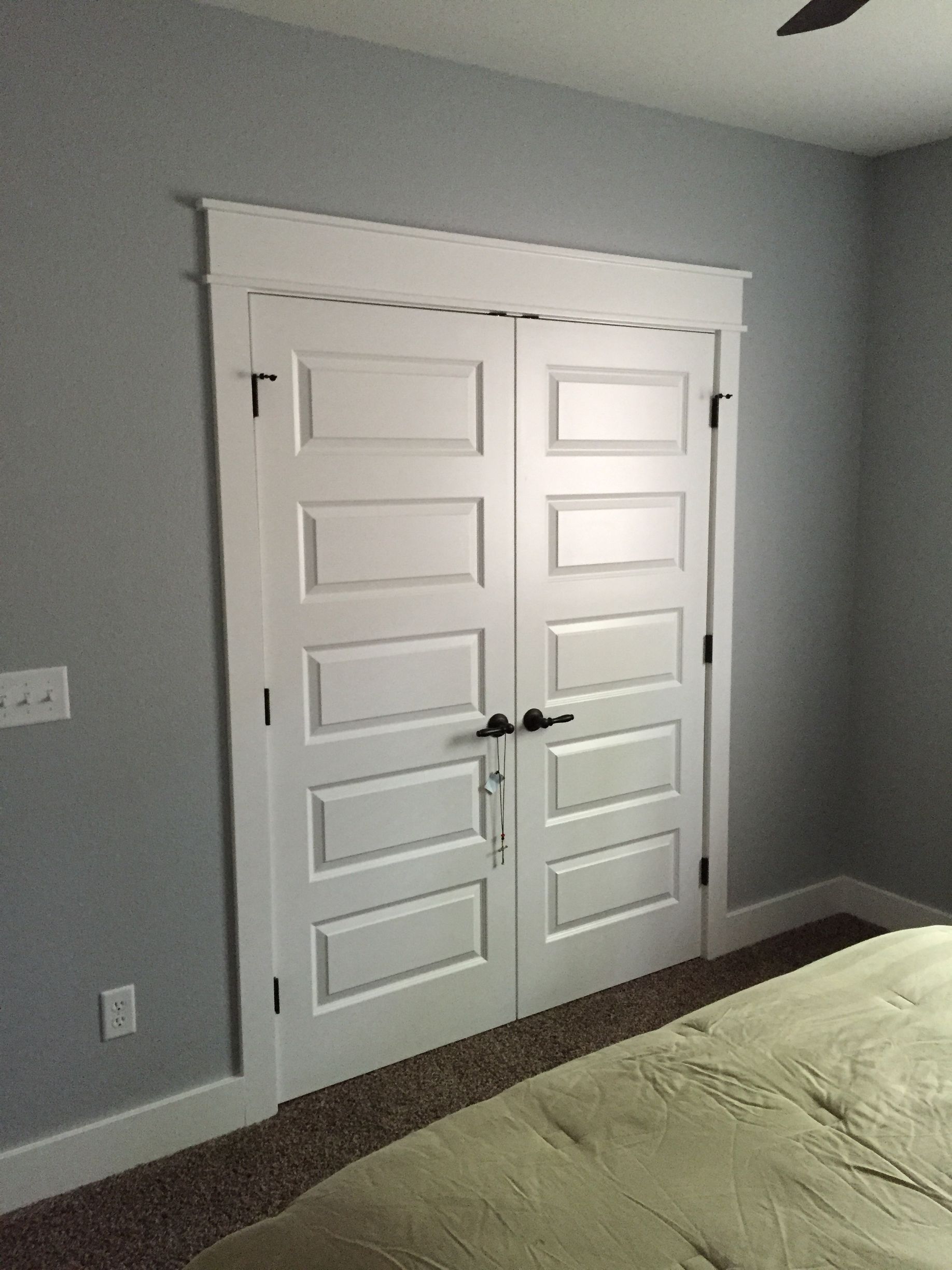 Bedroom with white double closet doors, gray walls, and carpeted floor next to a bed.