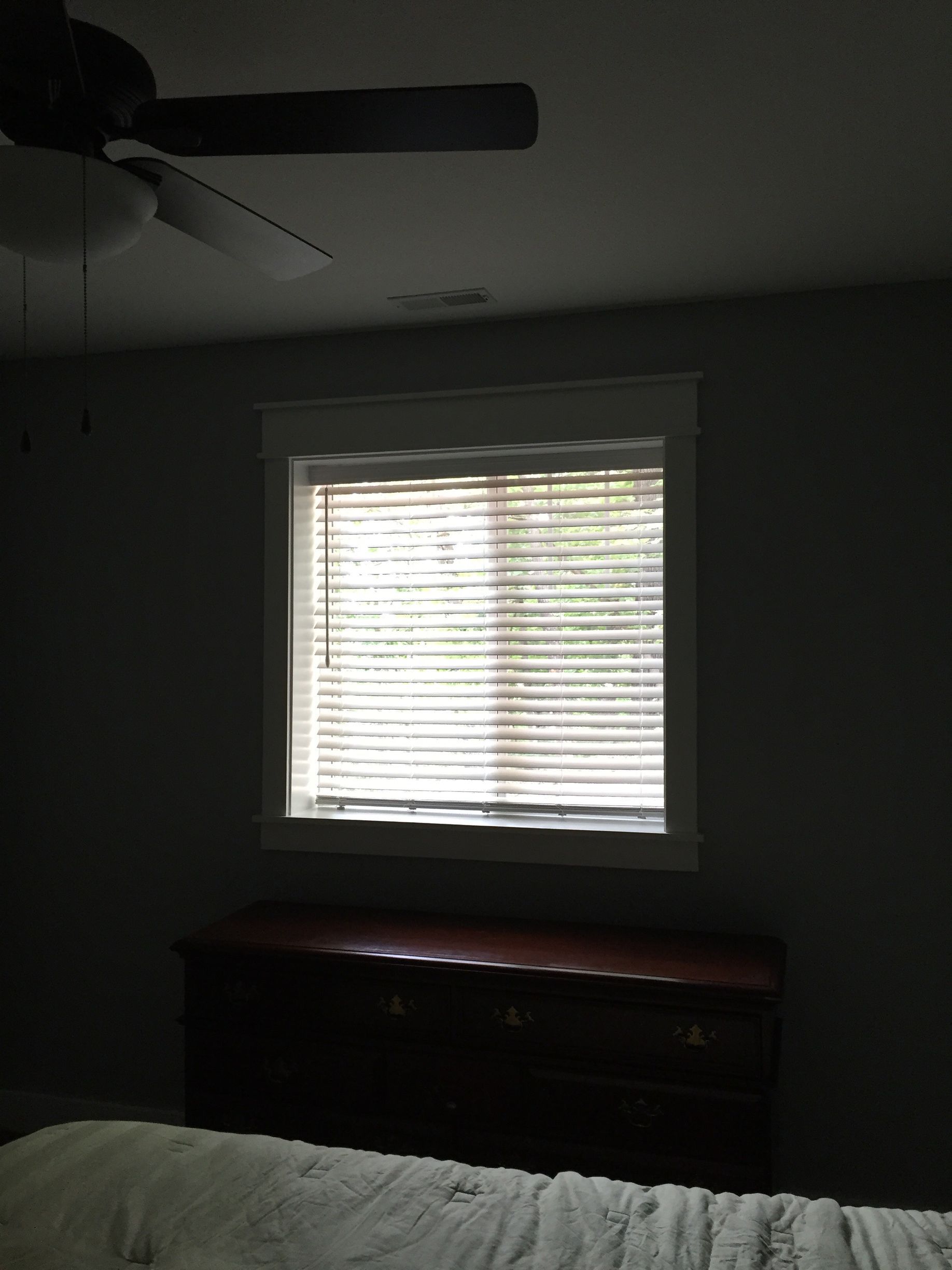 Dim bedroom with a window and blinds above a dresser, and a ceiling fan overhead.
