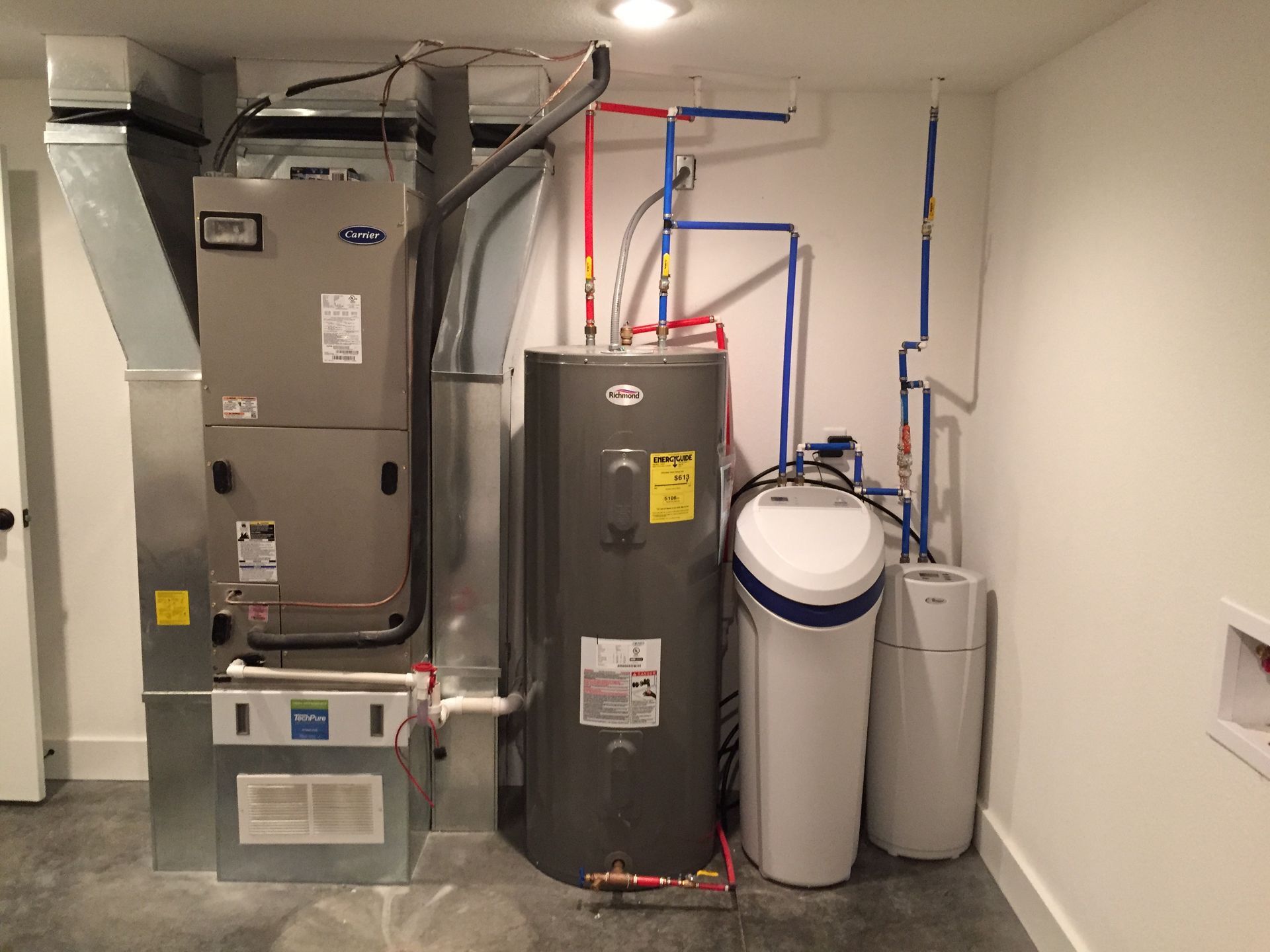 Utility room with furnace, water heater, and filtration tanks against a white wall.
