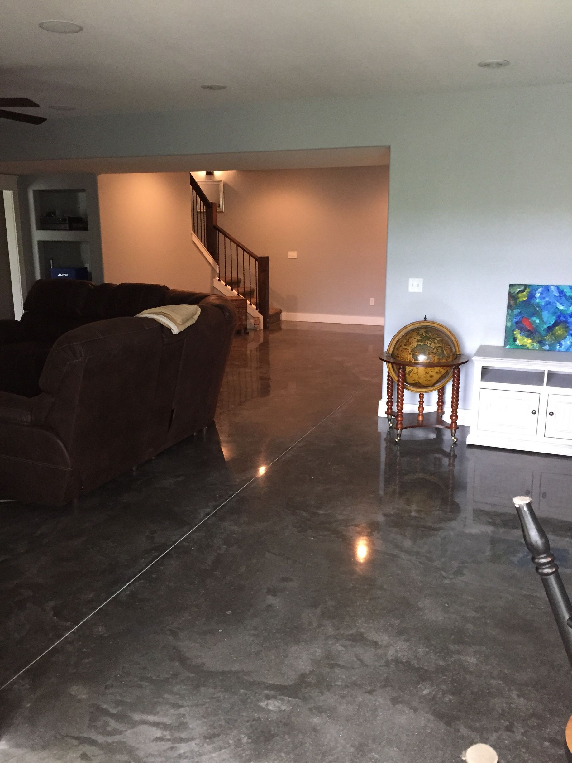 Living room with dark sofa, polished concrete floor, staircase, and small globe stand near white cabinet.