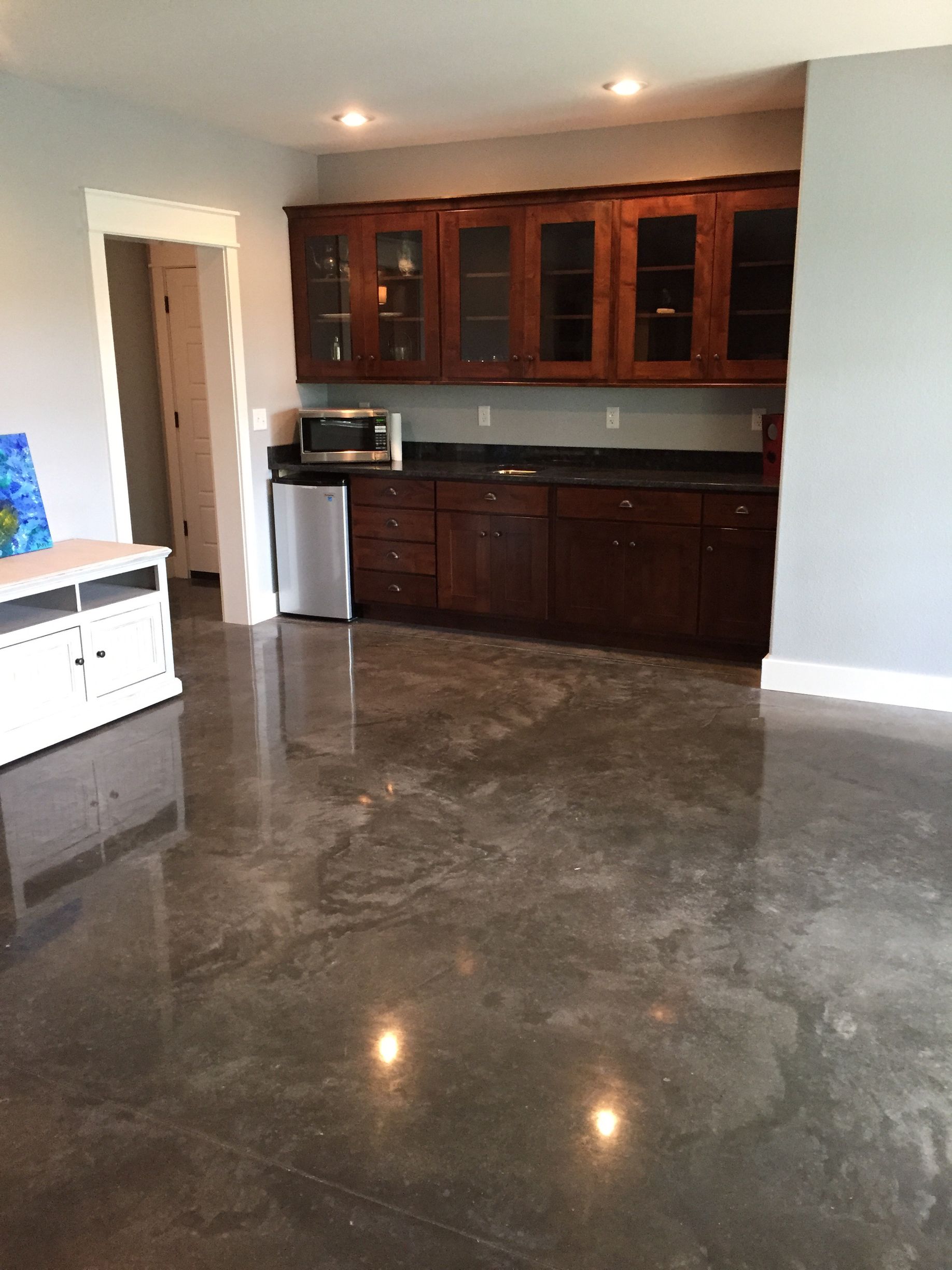 Modern kitchen with dark wood cabinets, stainless appliances, and polished concrete floor in an open room