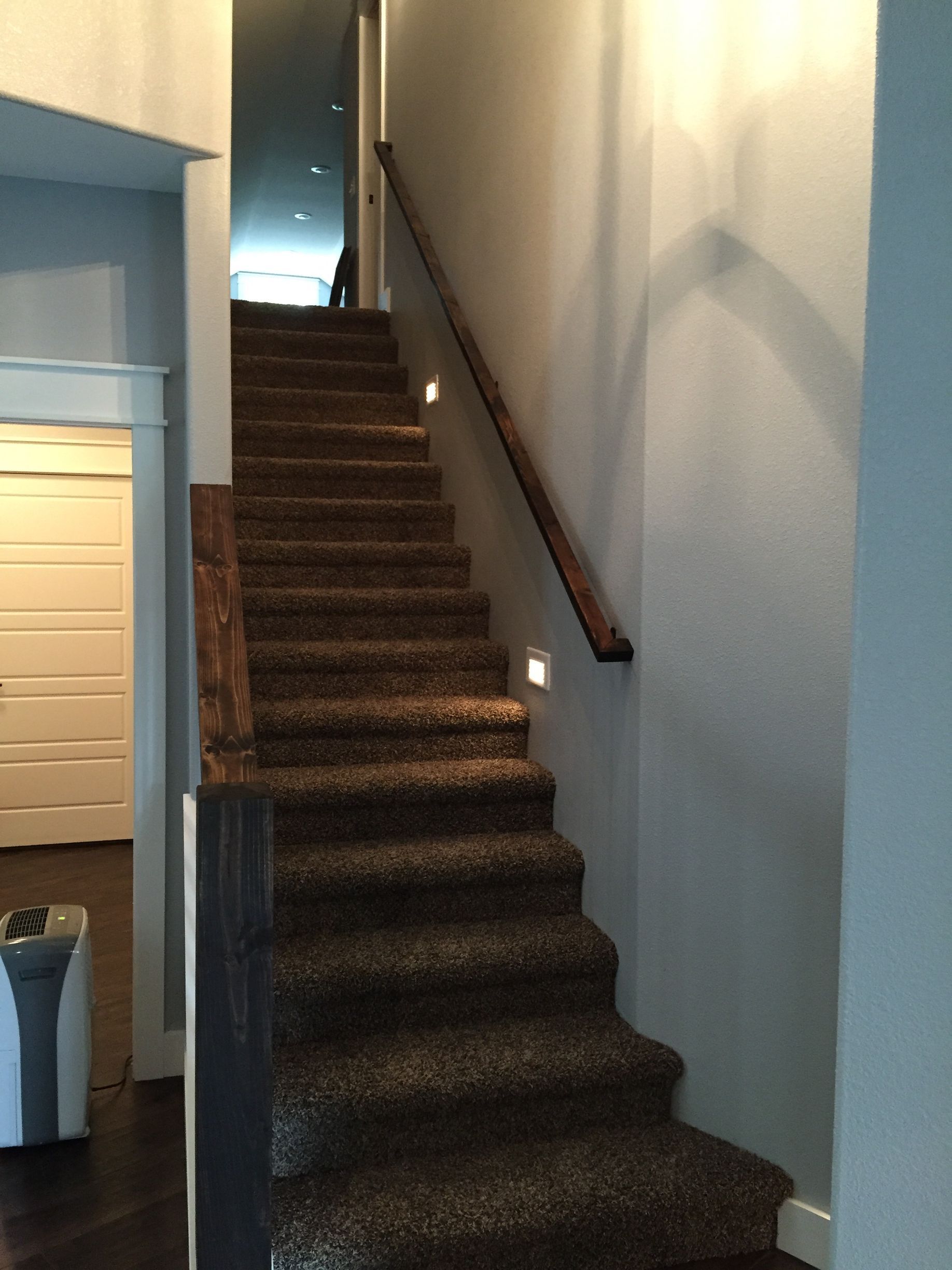 Indoor carpeted staircase with a wooden handrail in a narrow hallway.