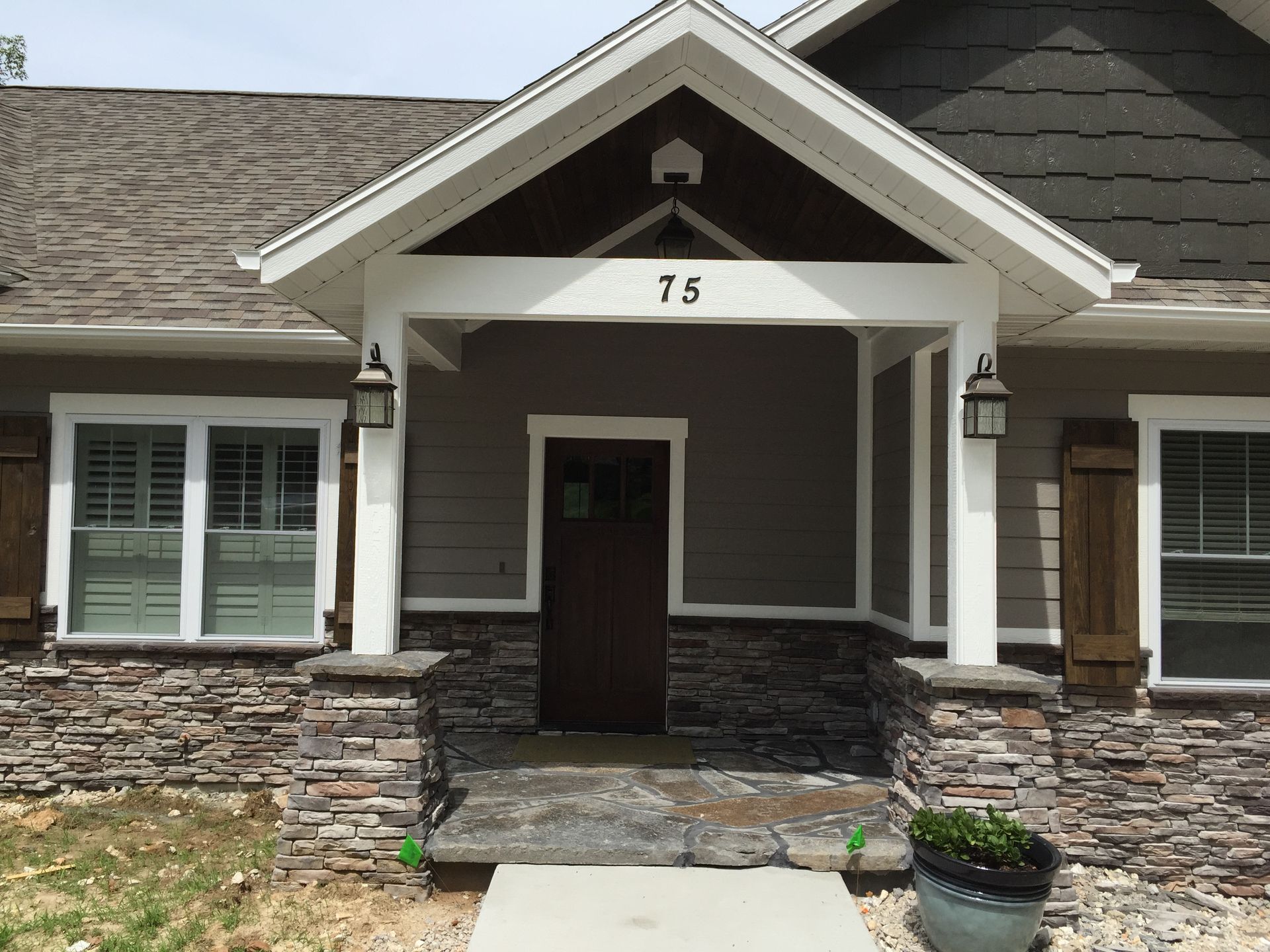 Front entrance of a house with stone siding, white trim, and a dark brown door marked 75