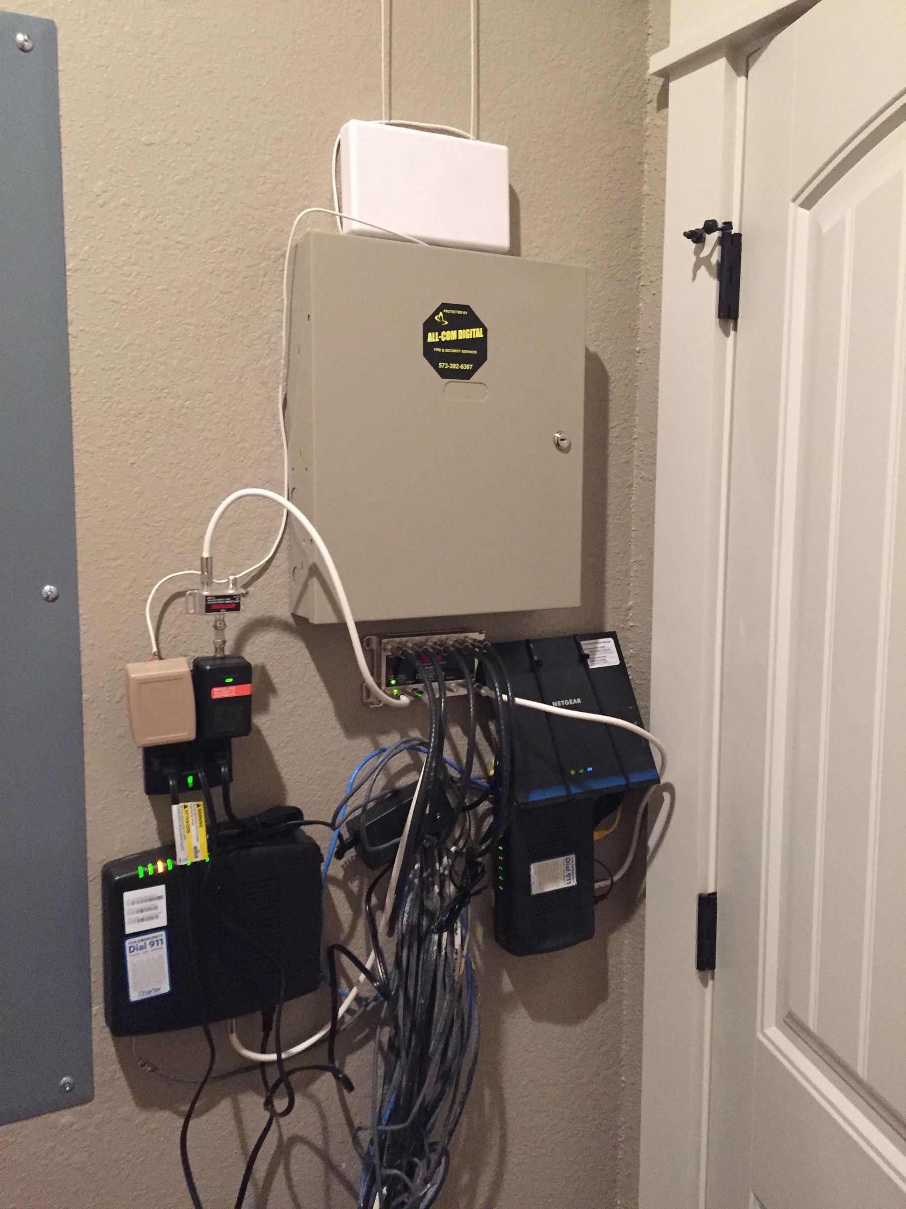 Wall-mounted home network equipment and cables beside a white door.
