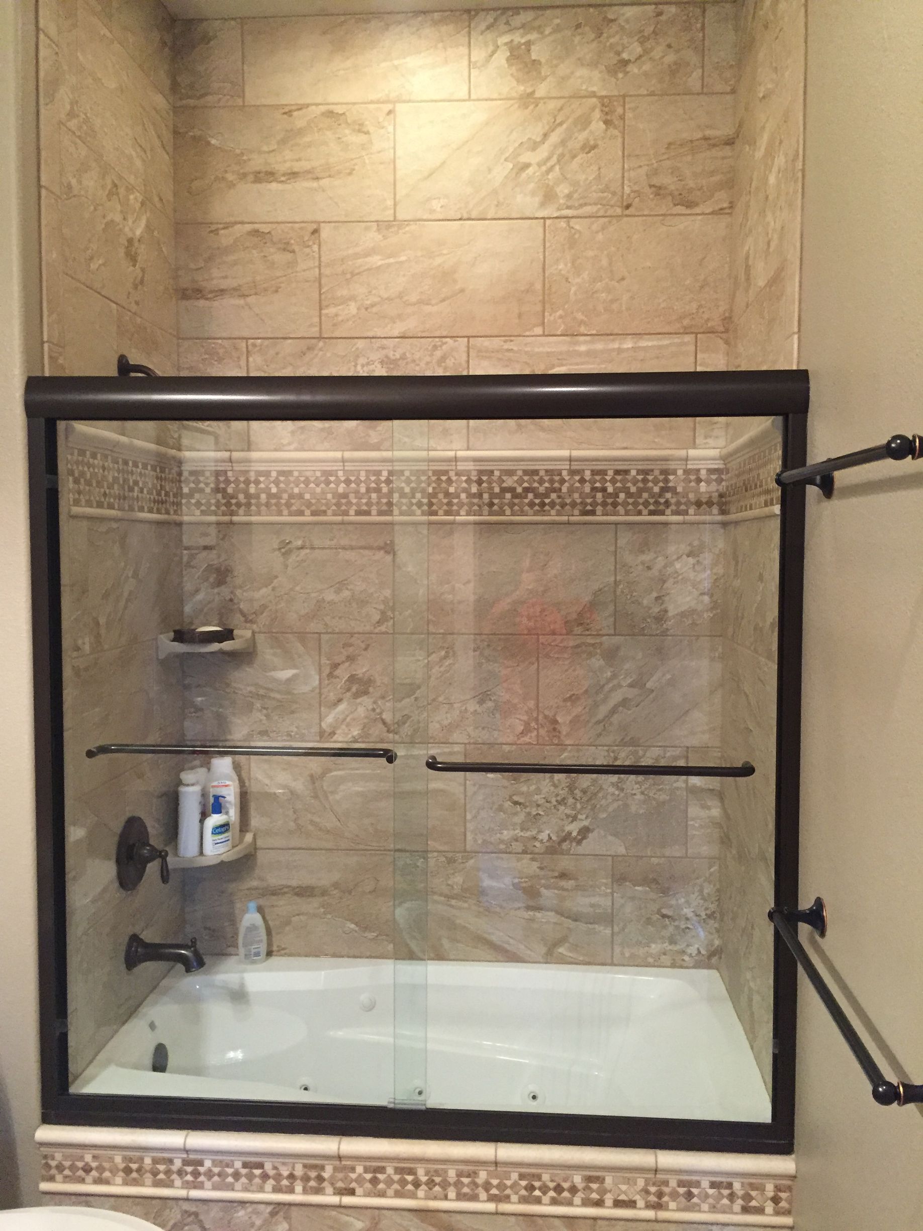 Empty glass shower stall with tiled walls and black metal frame in a bathroom.
