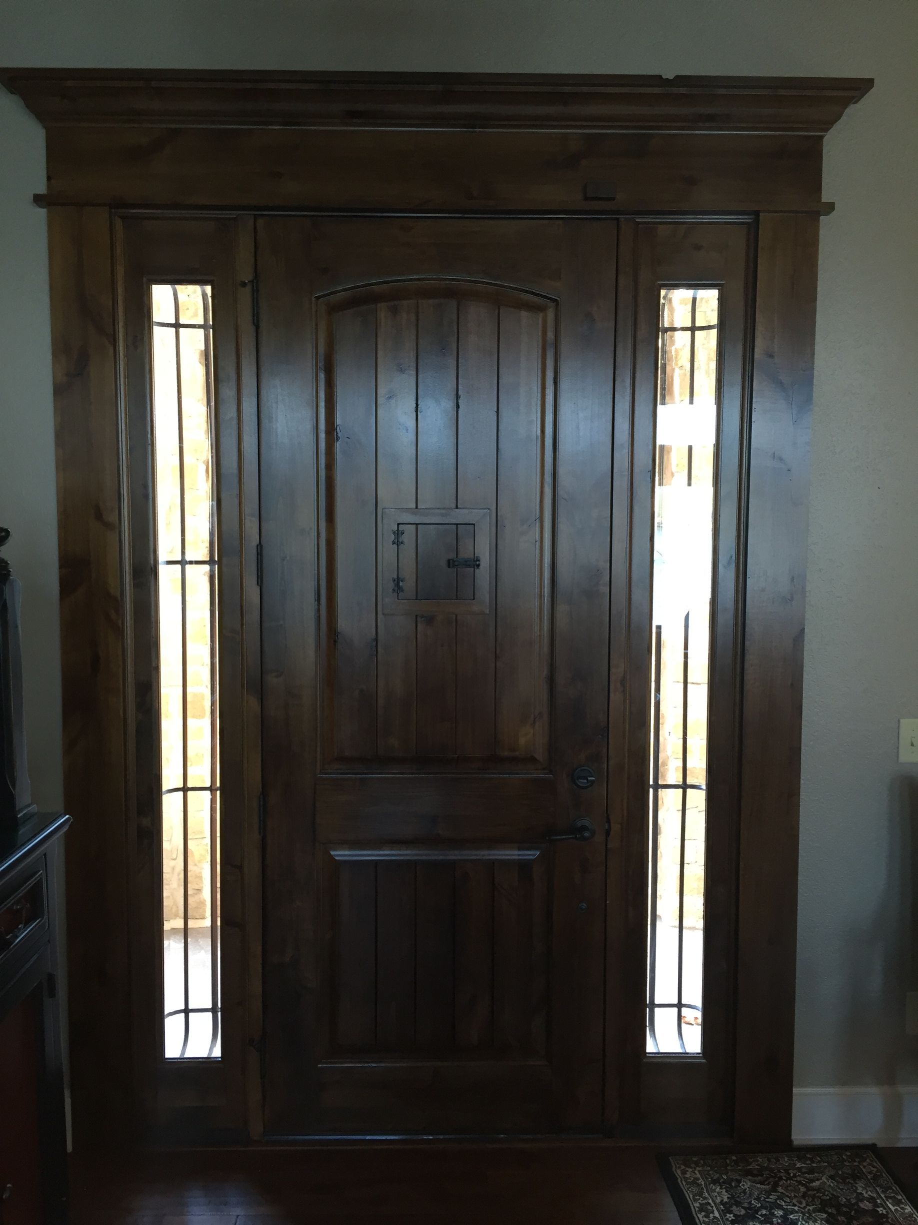 Wooden front door with decorative glass sidelights in a dim entryway