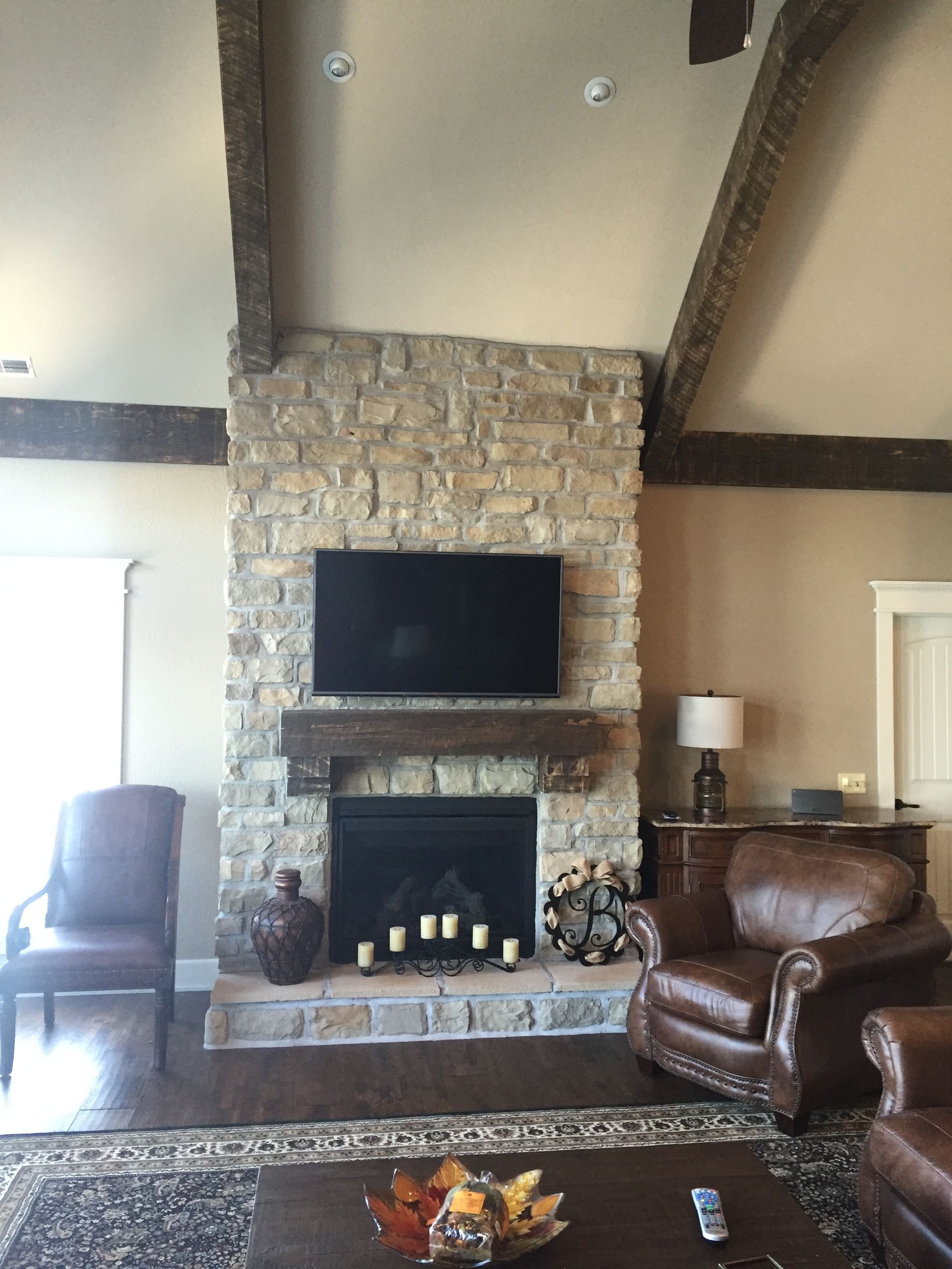 Living room with stone fireplace, mounted TV, leather chair, and wood beams.