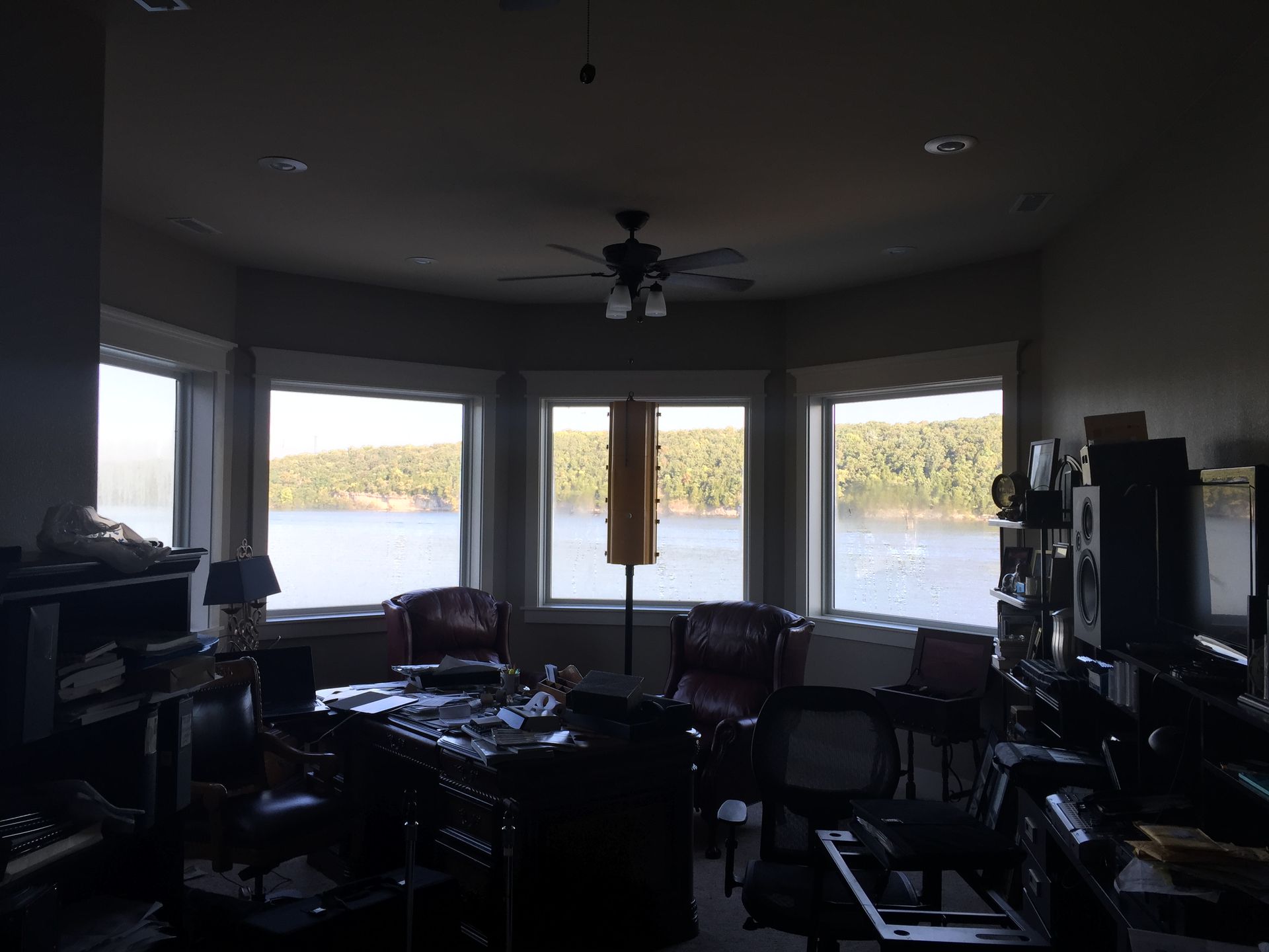Dim living room with large bay windows overlooking water and a ceiling fan overhead