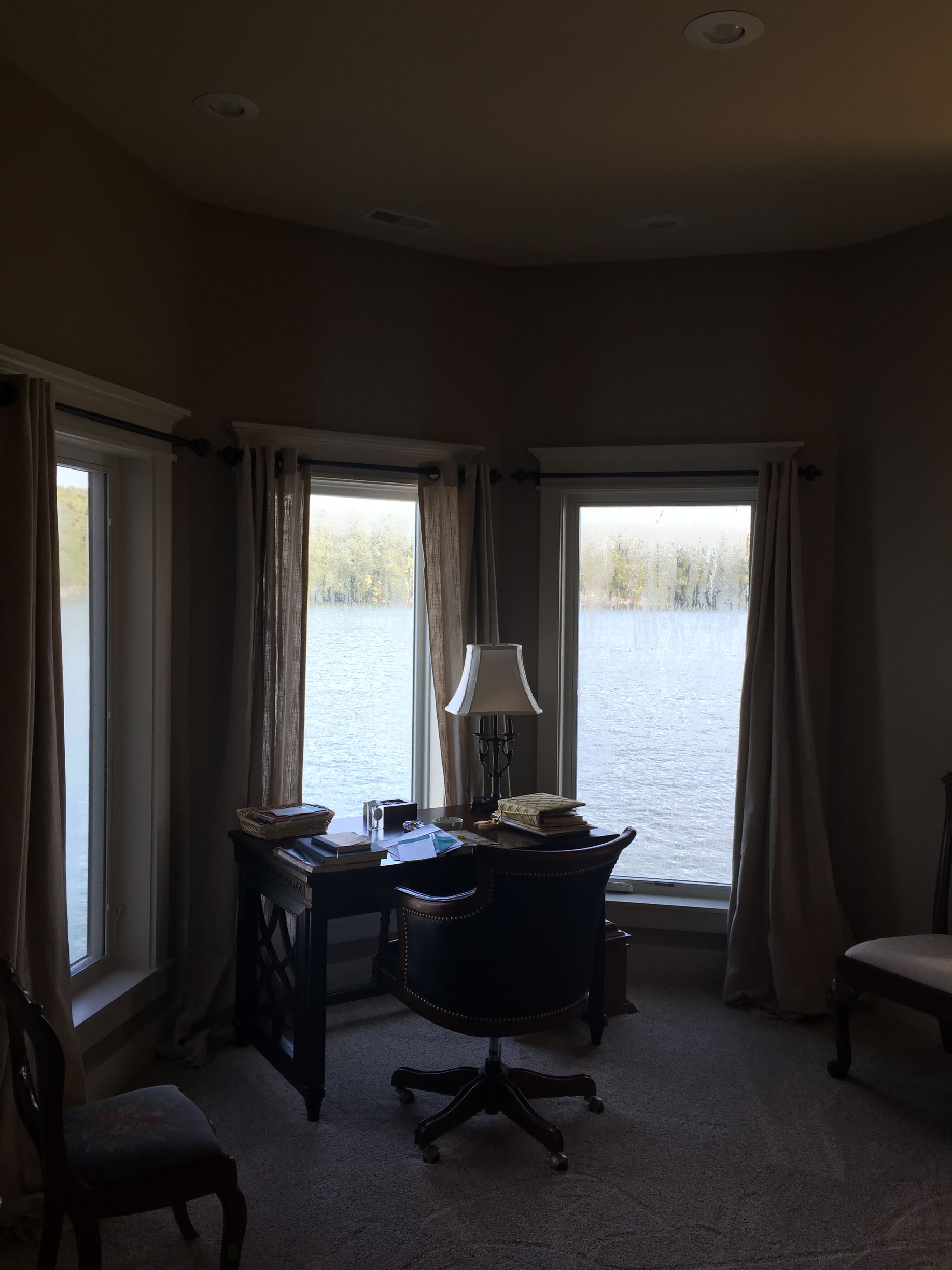 Small home office with desk, lamp, chair, and large windows overlooking a lake