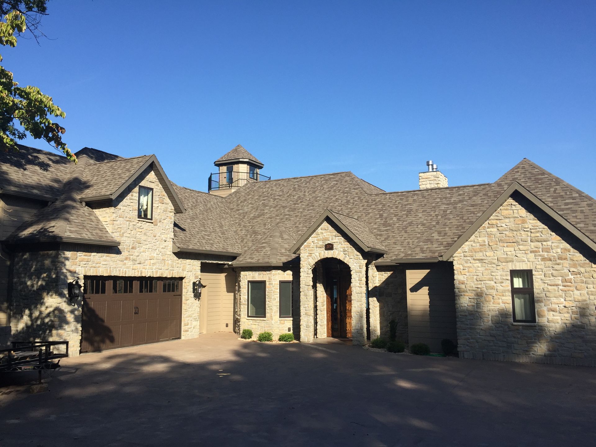 Stone house with arched entry, garage, and gabled roof under a clear blue sky