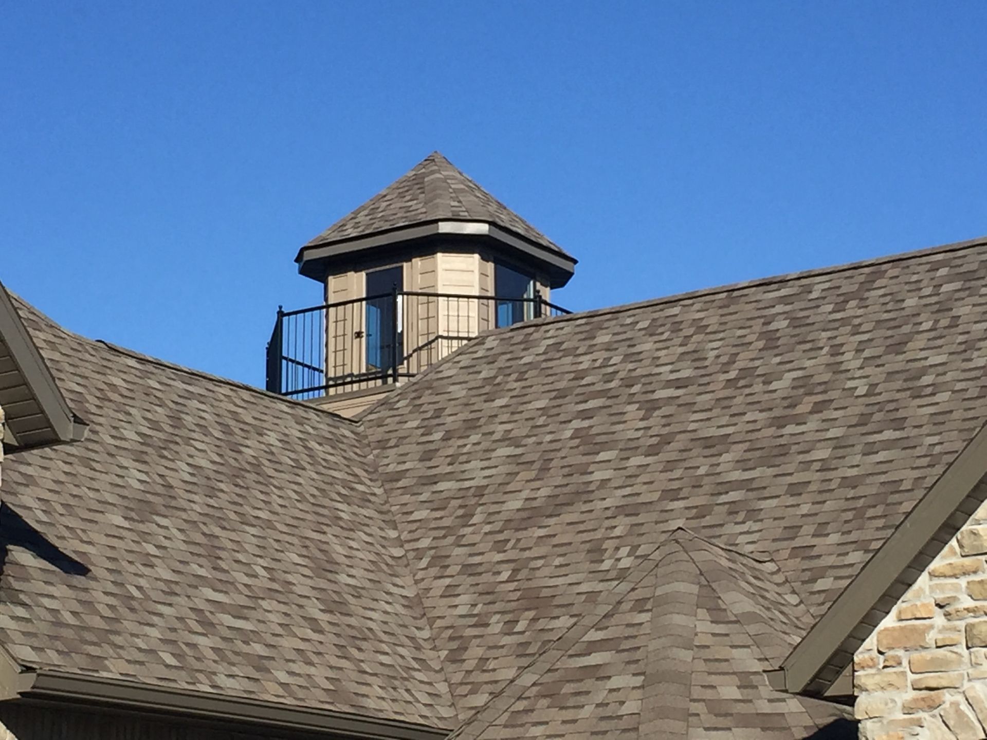 Roof with brown shingles and a small cupola against a clear blue sky