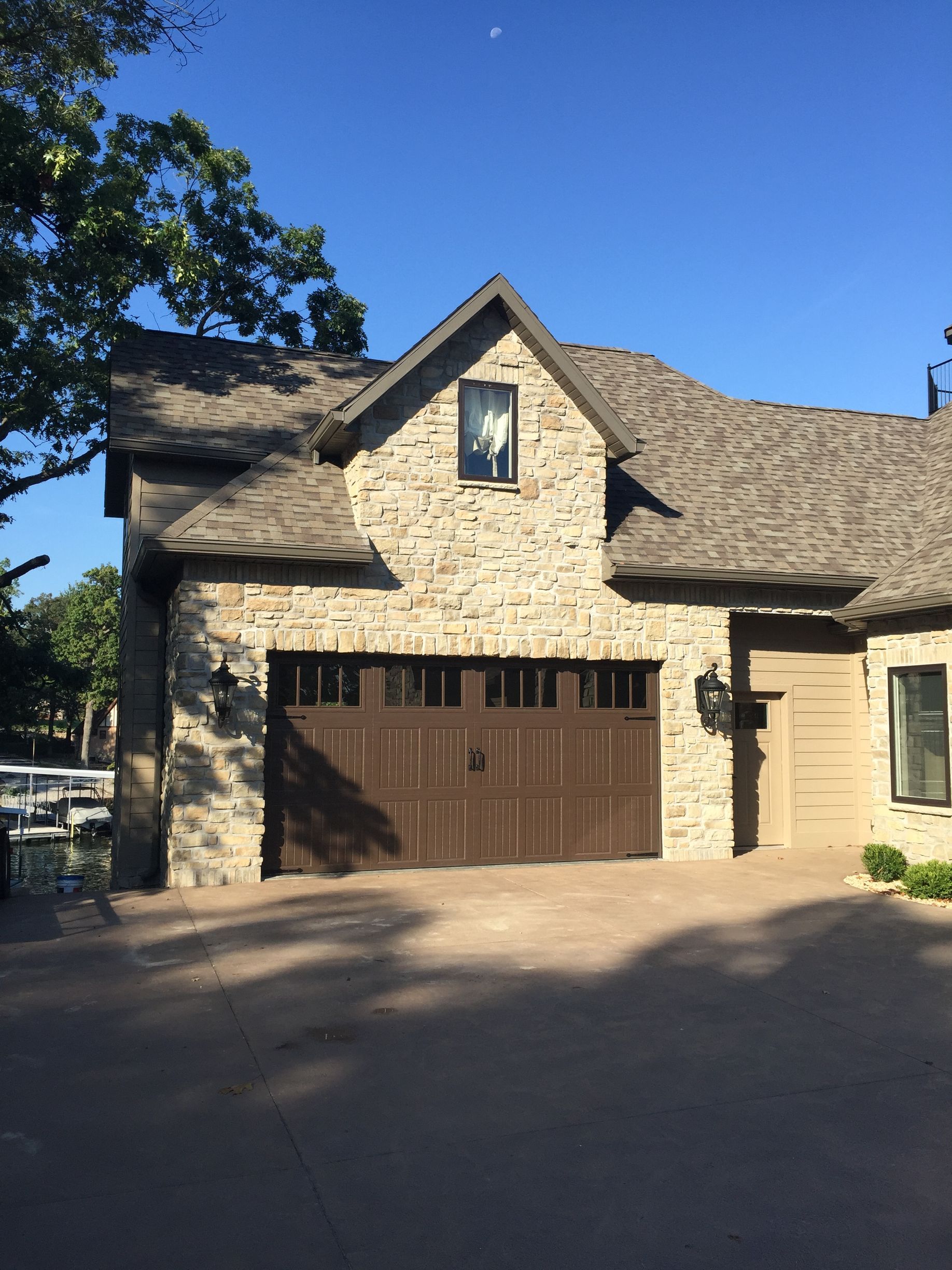 Stone house with brown garage door and blue sky, viewed from a driveway