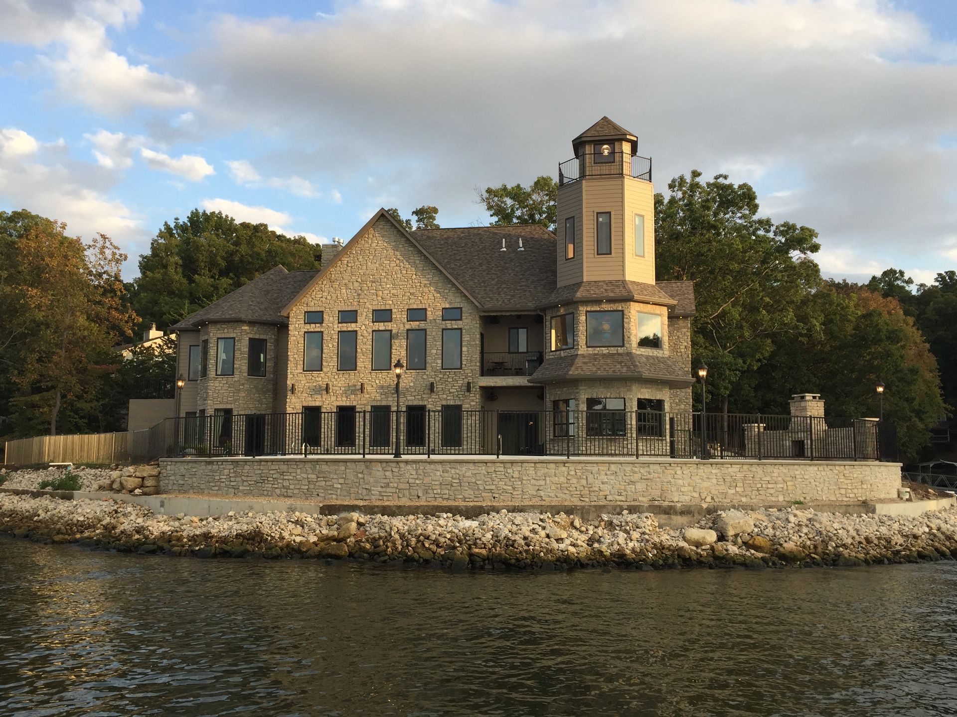 Stone house with a tower by the water, framed by trees and a cloudy sky