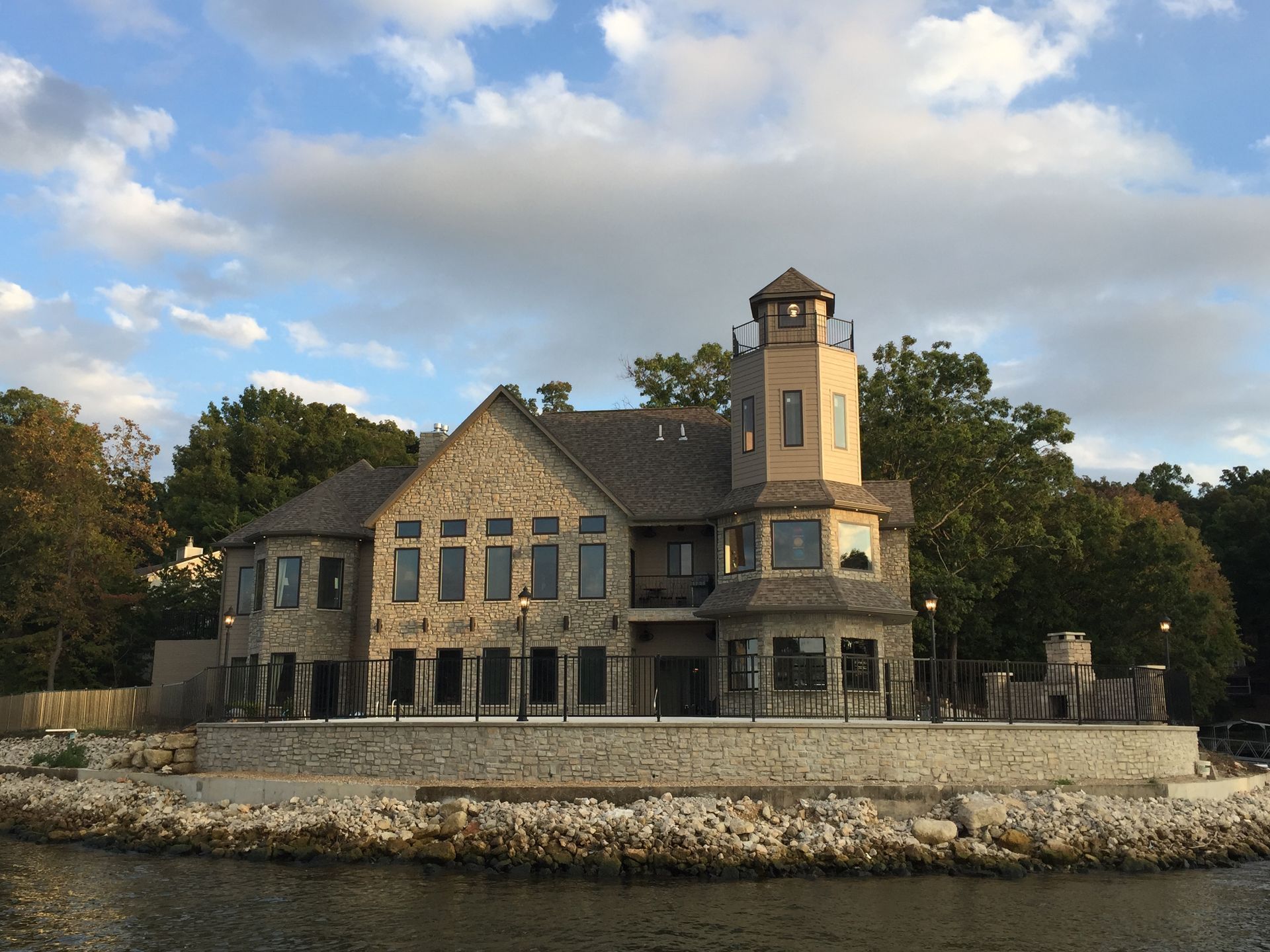 Stone waterfront mansion with turret and stone terrace under a cloudy sky