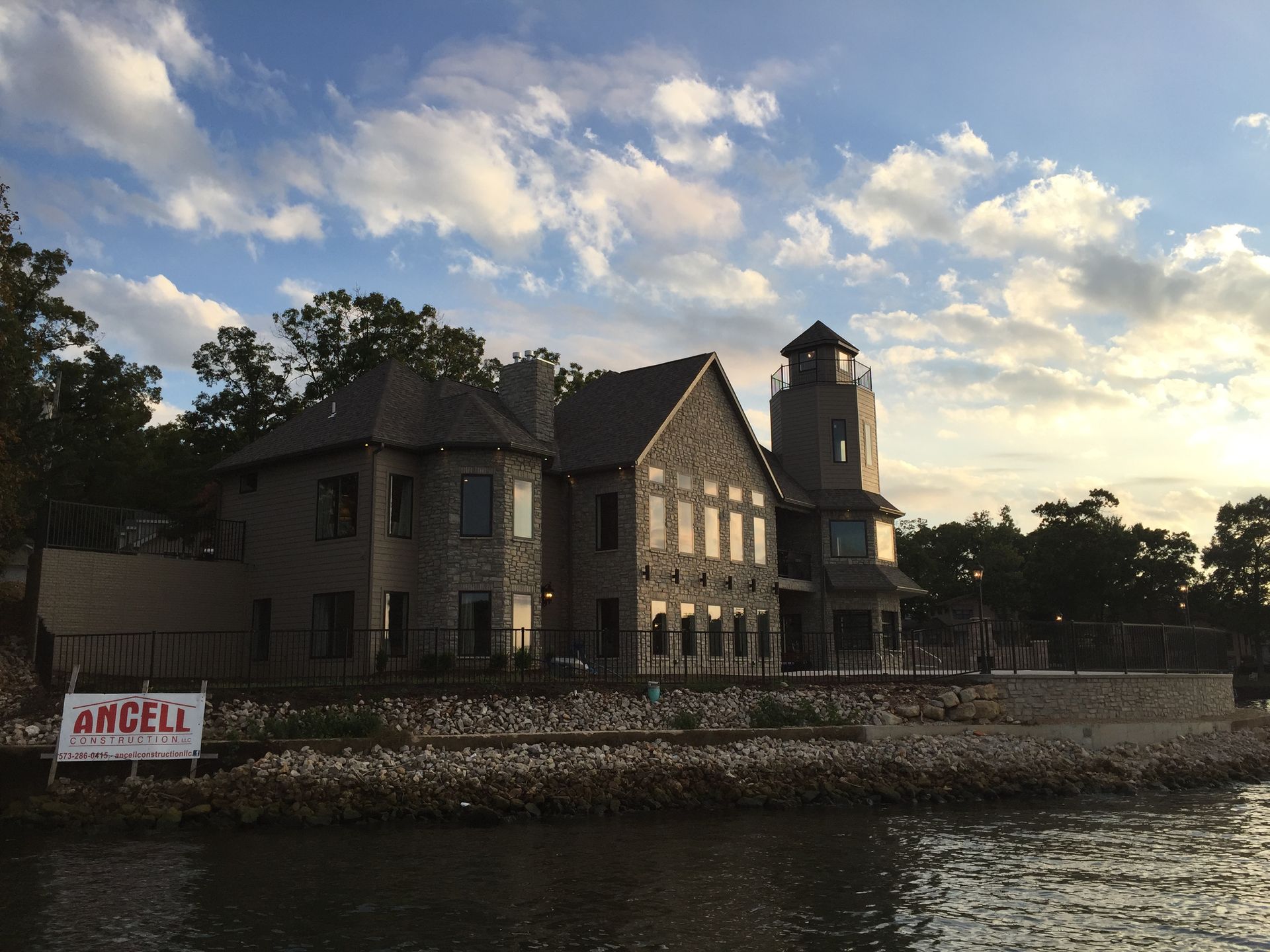Stone waterfront building at sunset with a small tower and cloudy sky, reflected on calm water