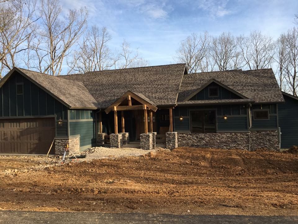 Dark green house with stone porch and garage, set against bare trees under a clear sky