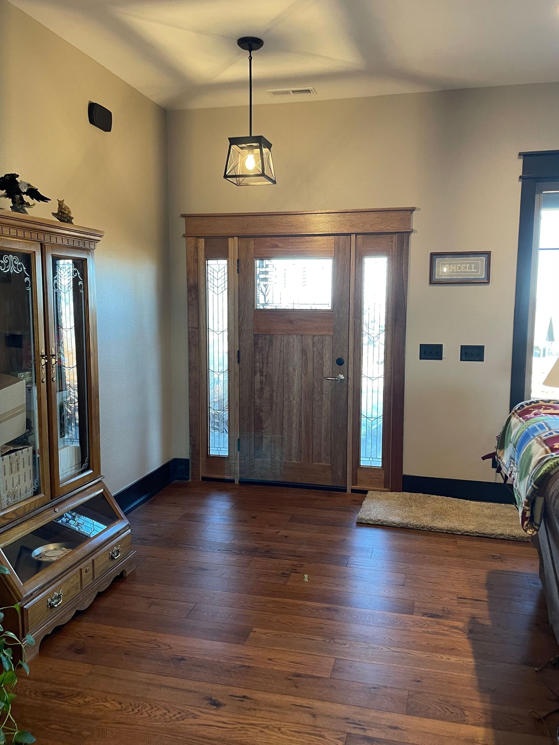 Sunlit entryway with wooden double doors, hardwood floors, and a large ornate mirror on the left.