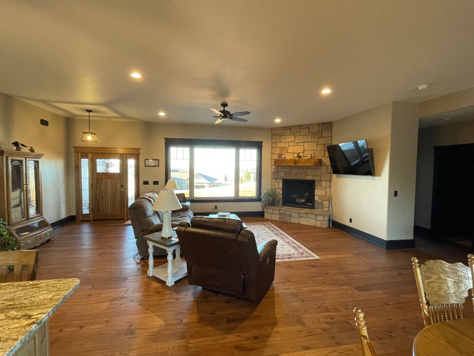 Spacious living room with brown leather chairs, stone fireplace, large windows, and hardwood floors