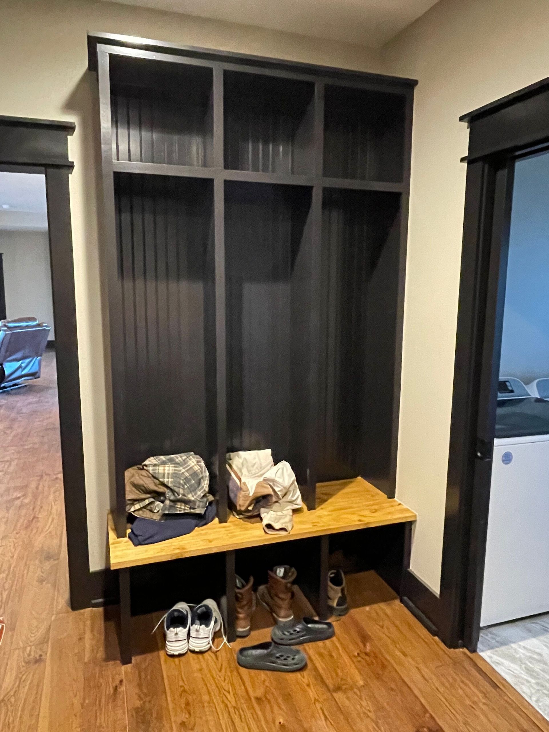 Dark wood entryway cubbies with shoes and bags on the floor beside an open front door.