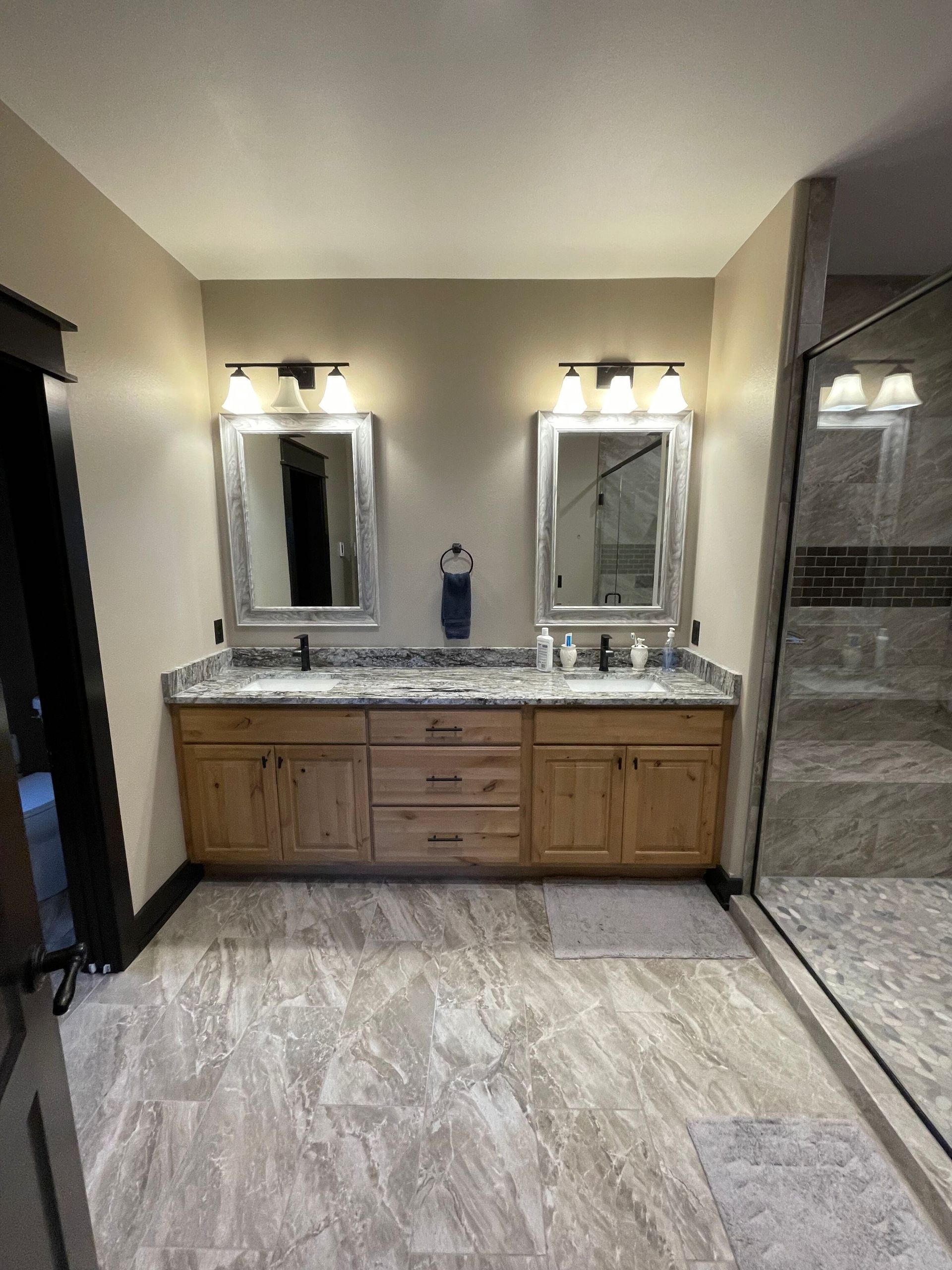 Bathroom vanity with double mirrors, stone countertop, and walk-in shower on the right