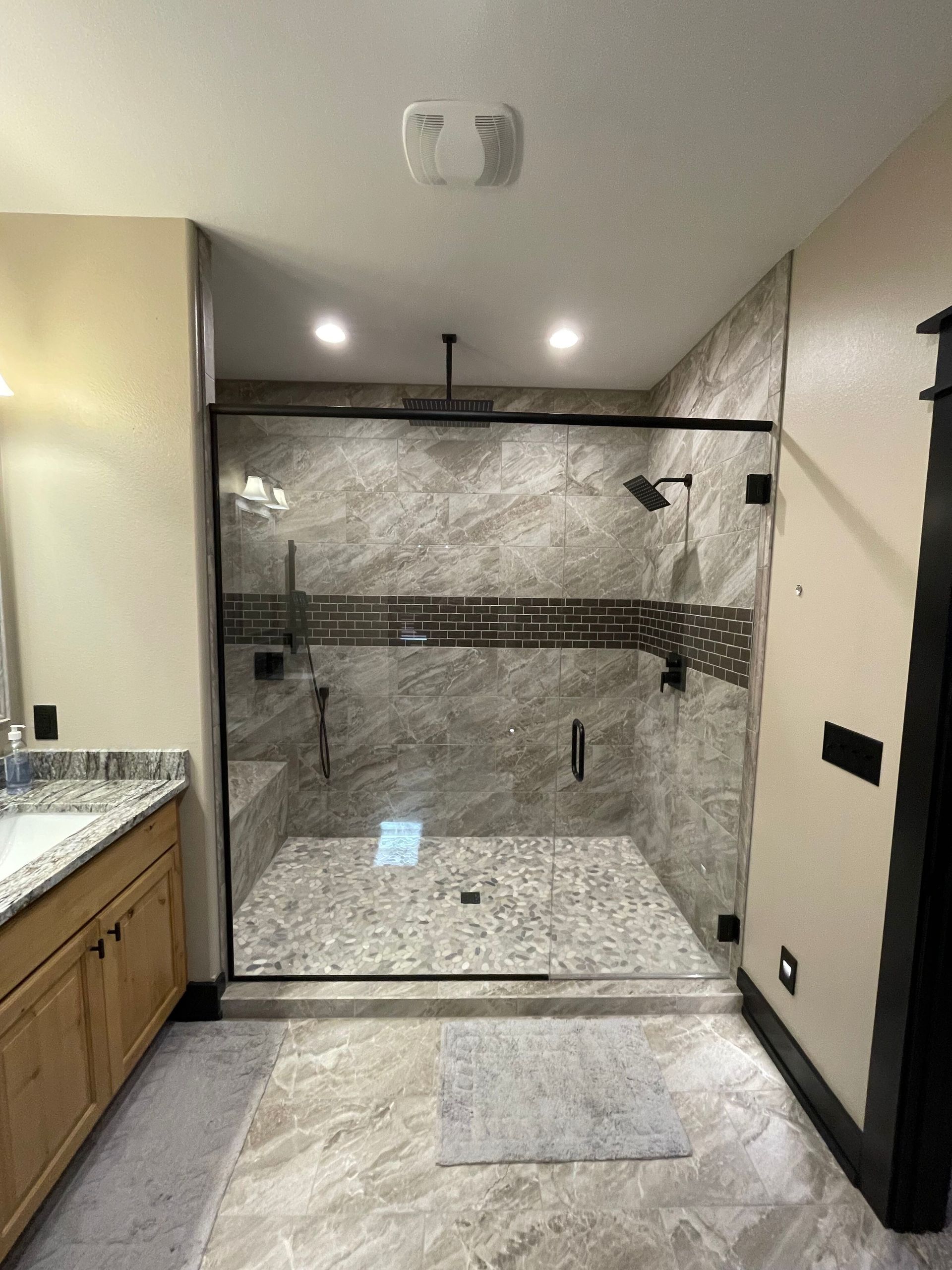 Modern walk-in shower with gray tile, glass enclosure, and black fixtures in a bathroom