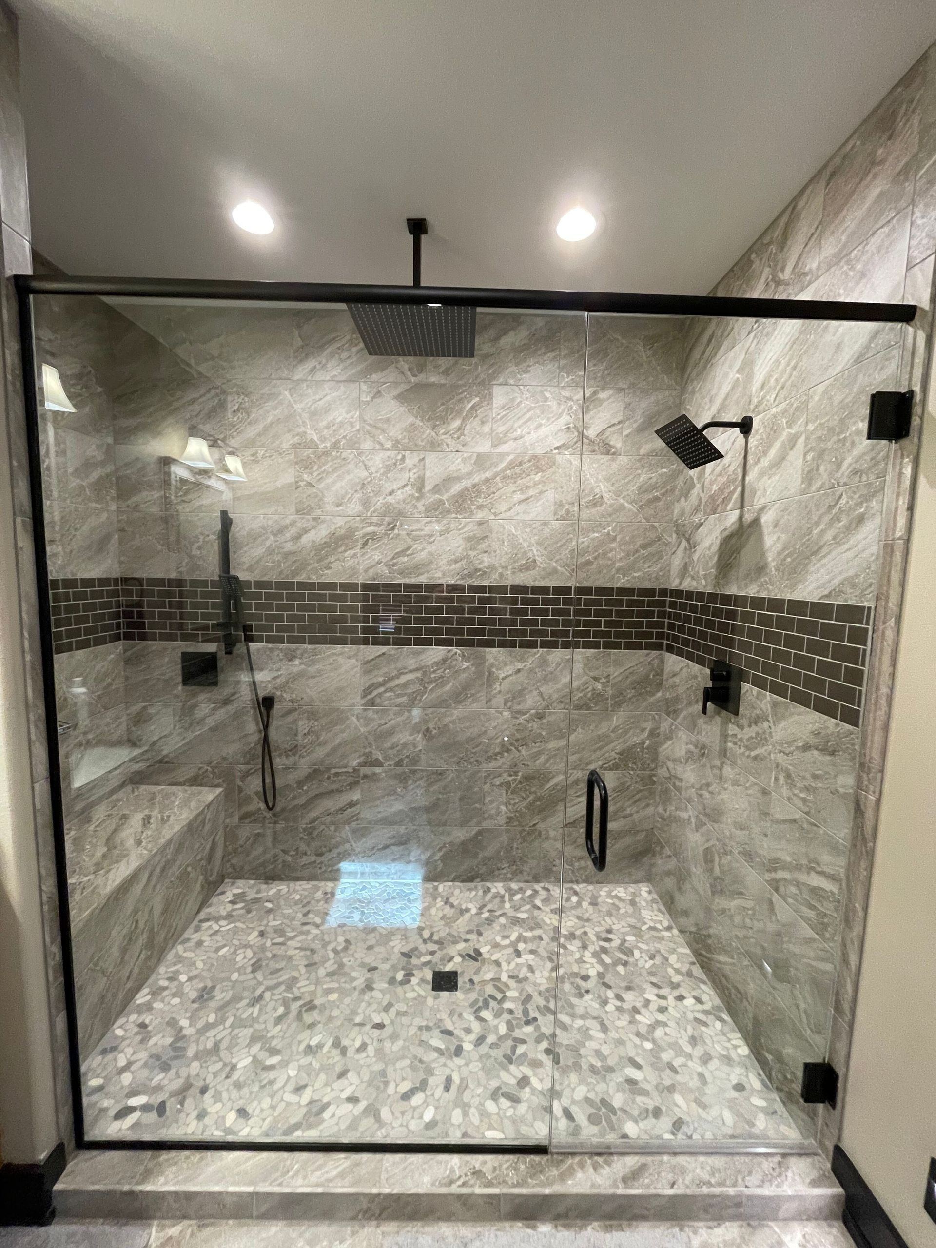 Modern walk-in shower with glass enclosure, marble tile, bench, and rainfall showerhead.