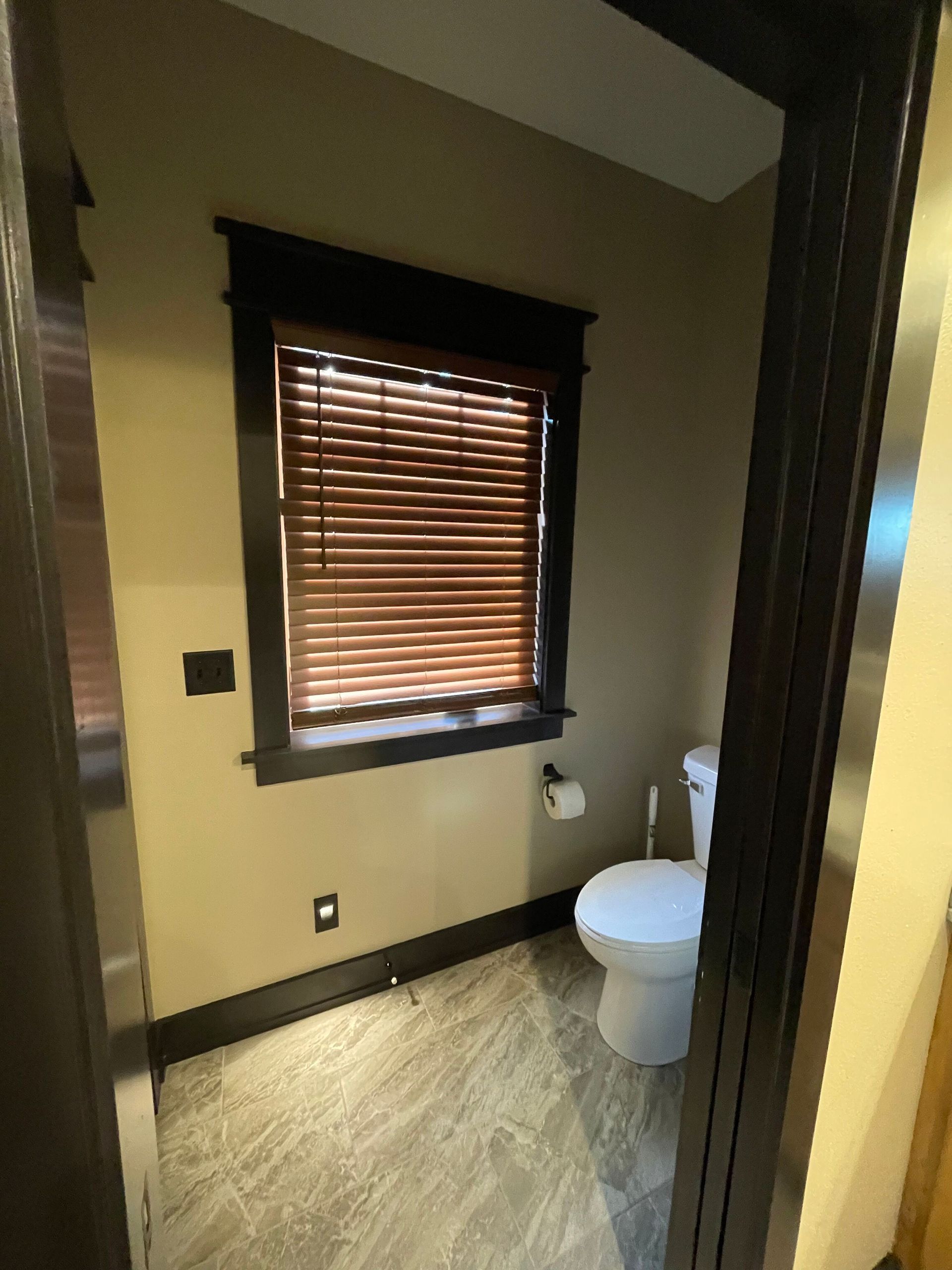 Small bathroom with a toilet, window blinds, beige walls, and wood-look flooring.
