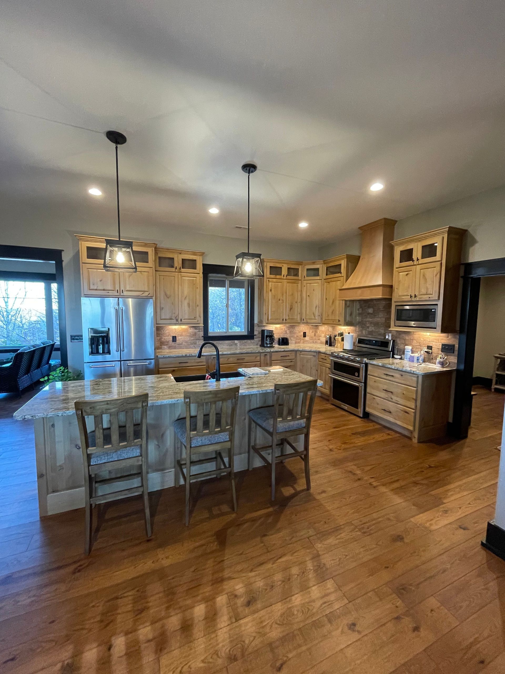 Spacious kitchen with wood cabinets, island, pendant lights, and dining table on hardwood floor.