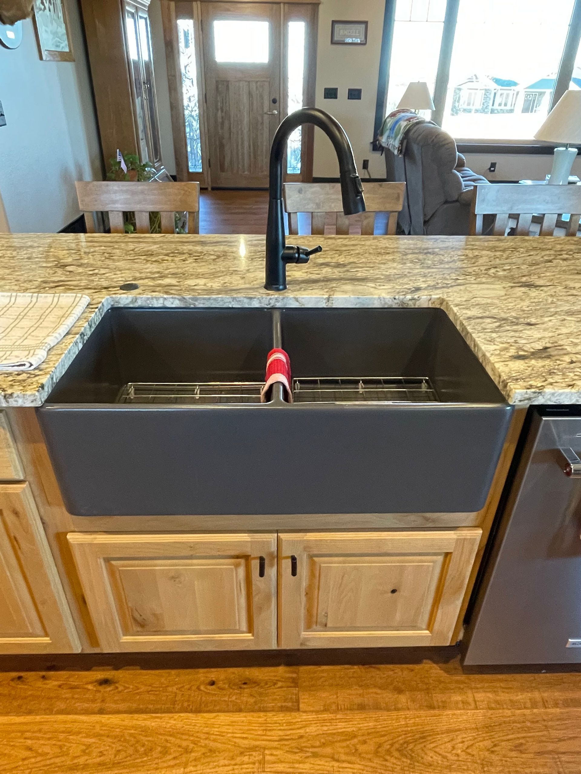 Kitchen sink with black faucet and dark apron front, set in a granite countertop with wood cabinets.