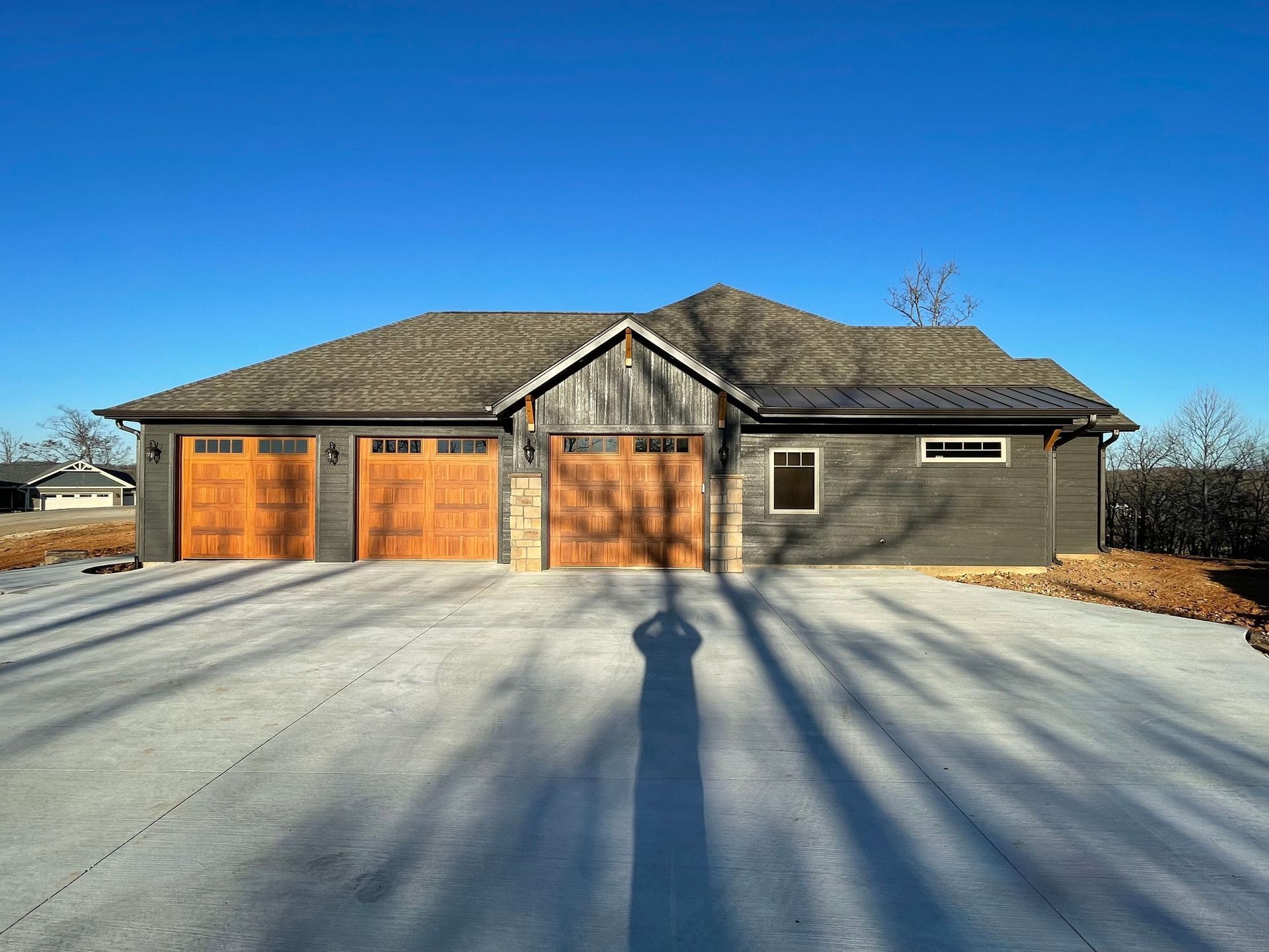 Single-story house with three orange garage doors under a bright blue sky, long shadows on snowy driveway