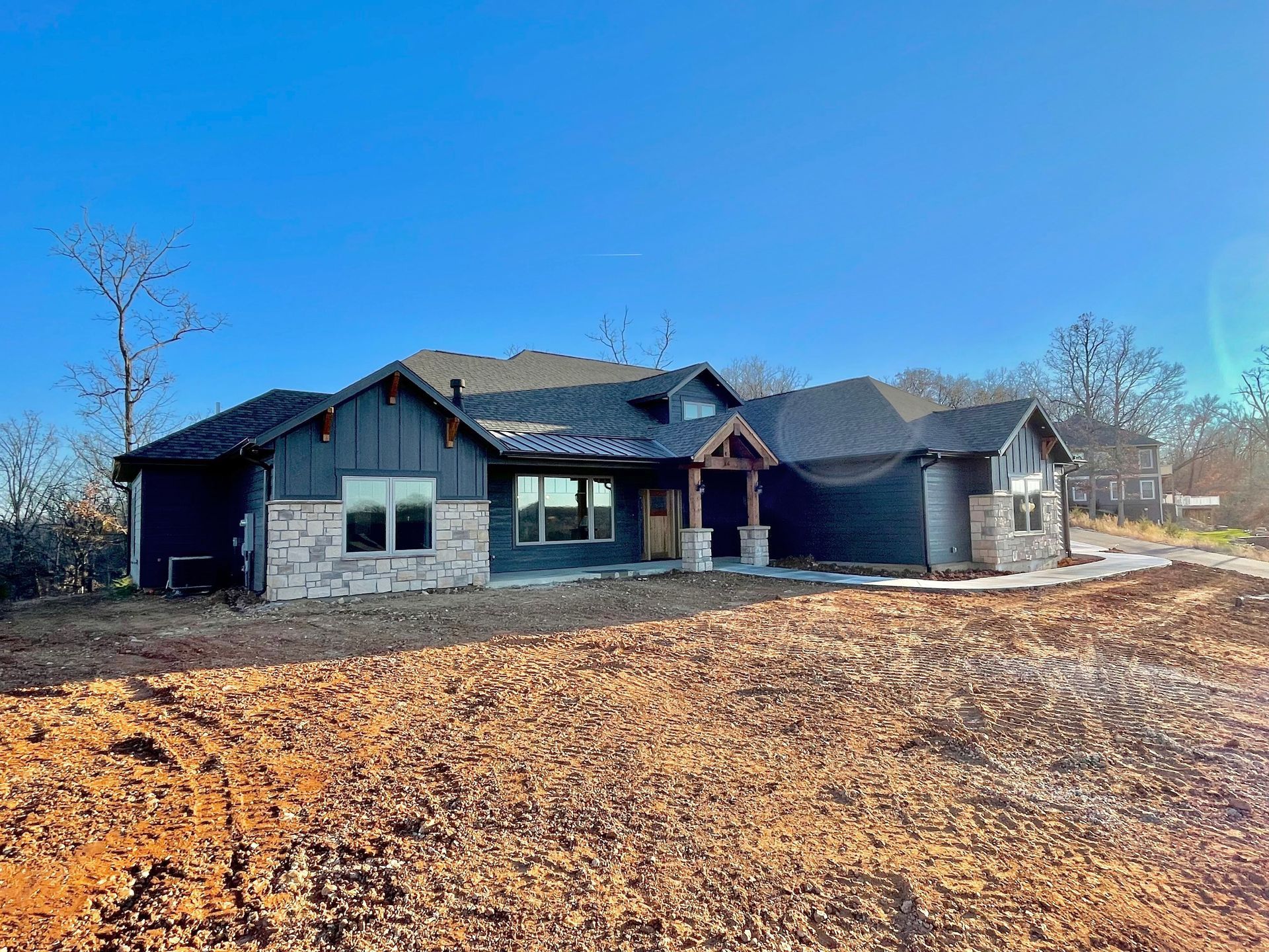 Newly built modern house with dark siding on a bare lot under a clear blue sky