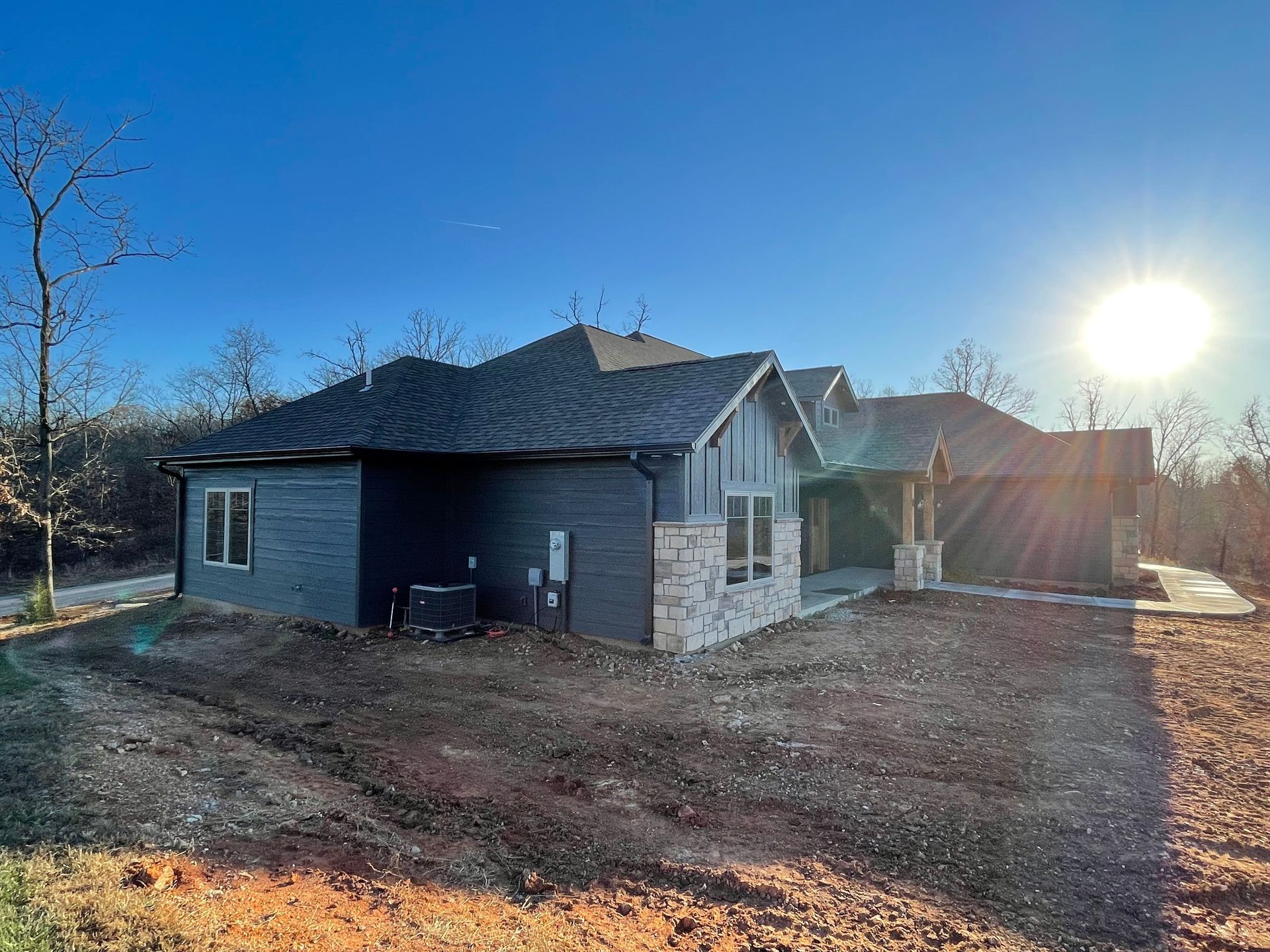 New single-story house under construction at sunset, with blue-gray siding and a dirt lot