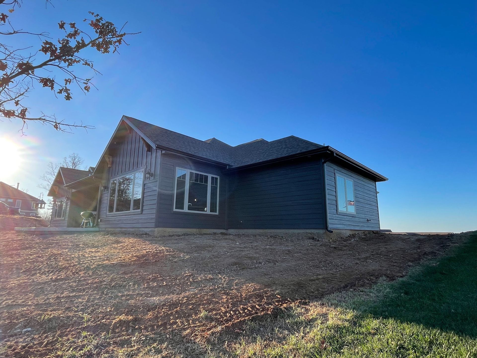 Single-story gray house on a sloped dirt lot under a clear blue sky at sunset