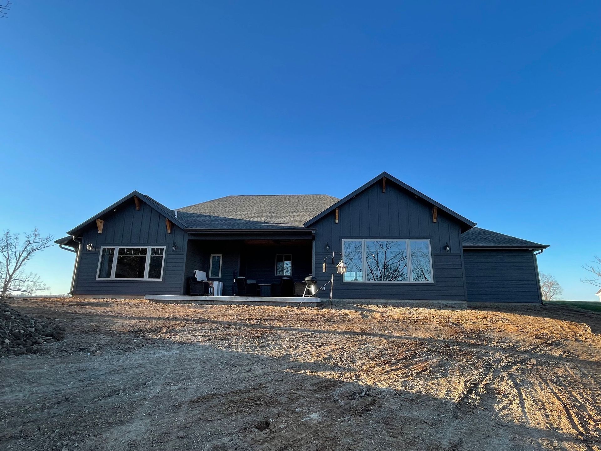 Dark blue farmhouse under construction on a dirt lot beneath a clear blue sky