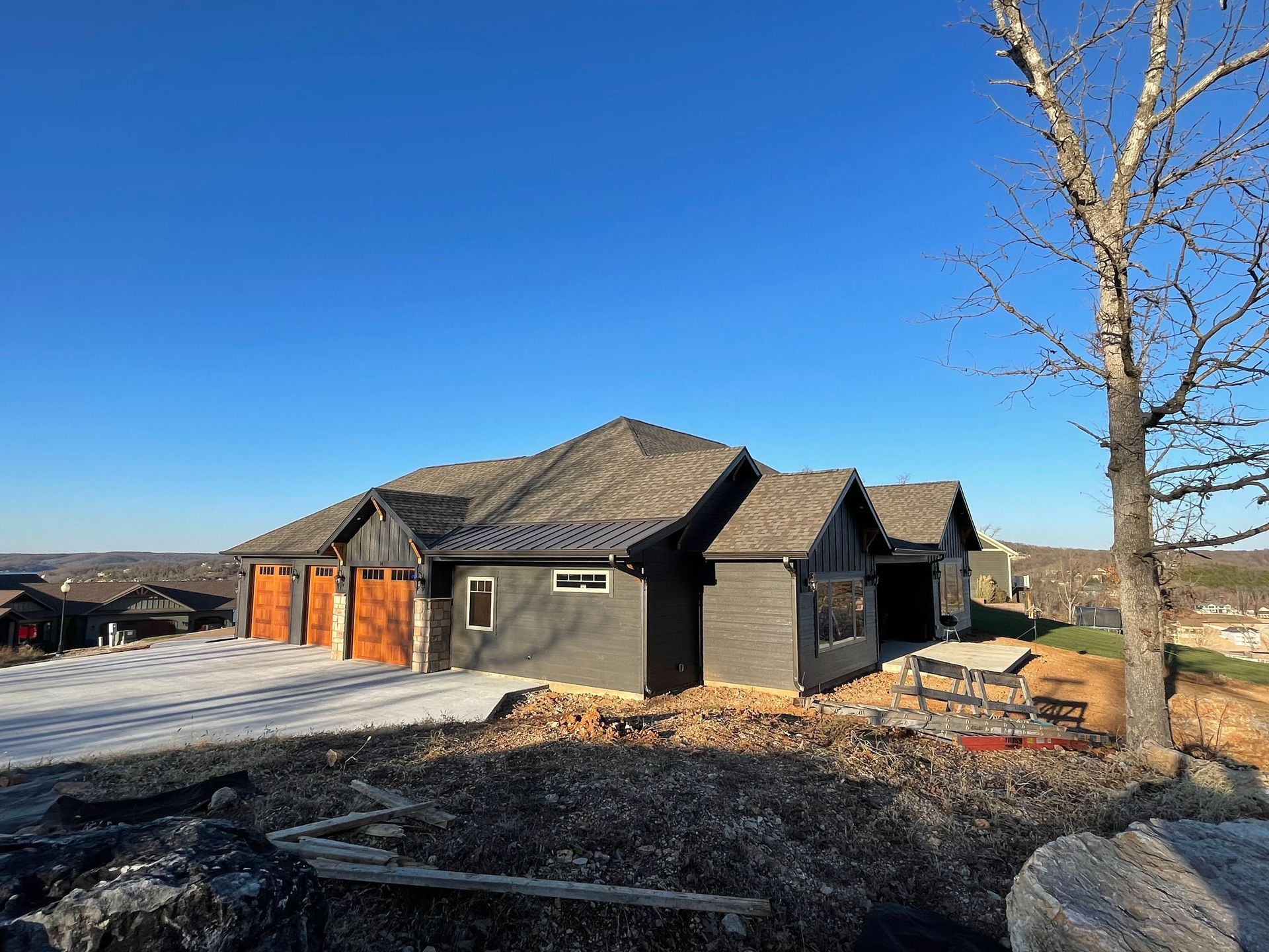 Modern black house with orange garage doors on a snowy rural lot under a clear blue sky