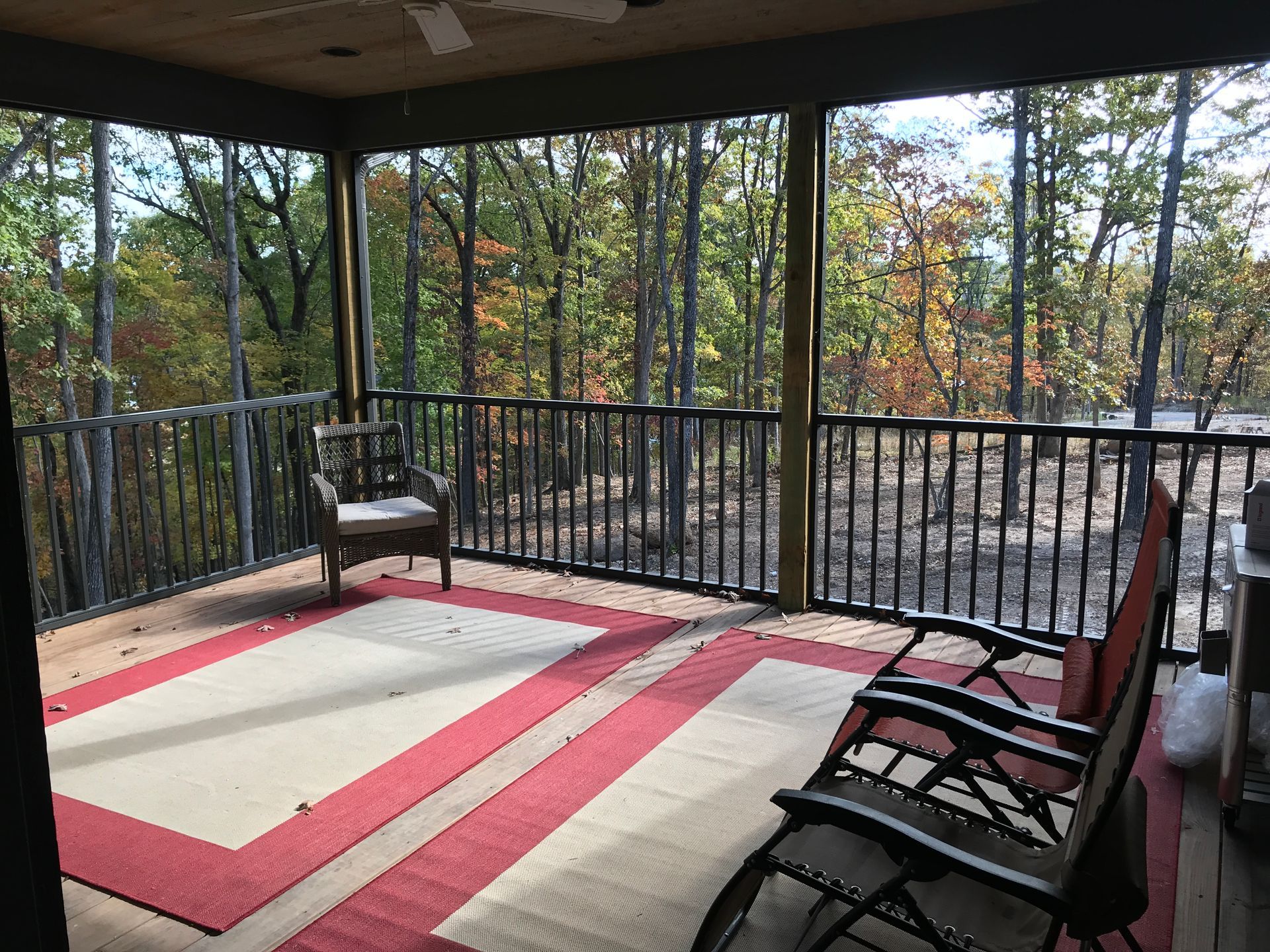 Covered deck with chairs and a red-and-cream rug overlooking a wooded view