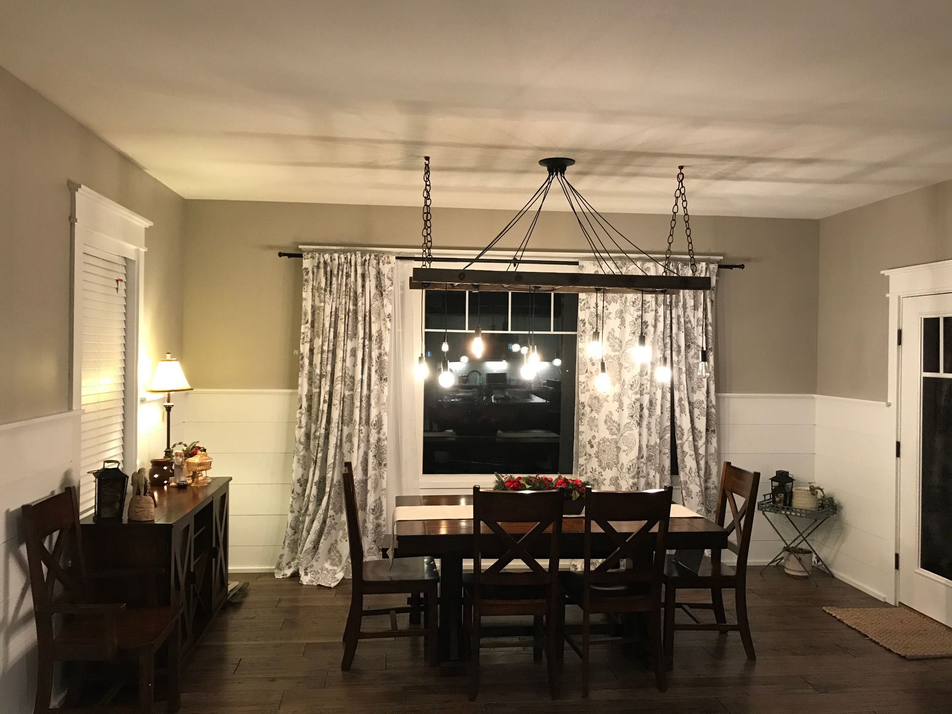 Dining room with dark wood table and chairs, curtains framing a window, and a sideboard along the wall.