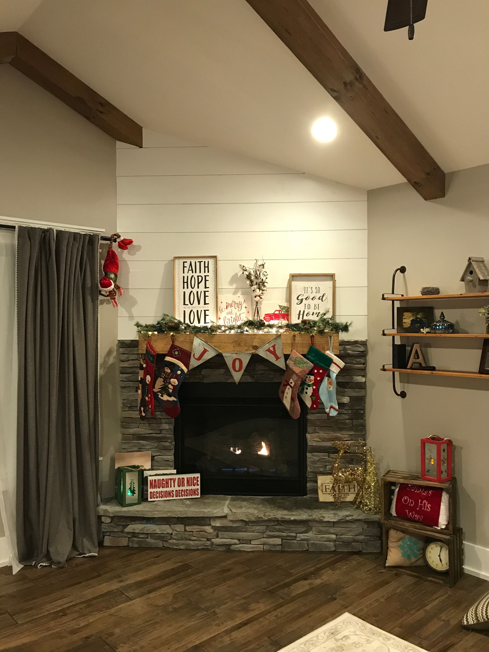 Cozy living room with stone fireplace, holiday garland, gray curtains, and wood ceiling beams