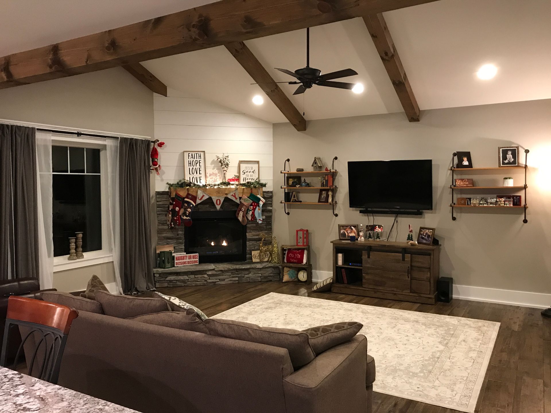 Cozy living room with stone fireplace, wall-mounted TV, brown sofa, and vaulted ceiling with exposed beams