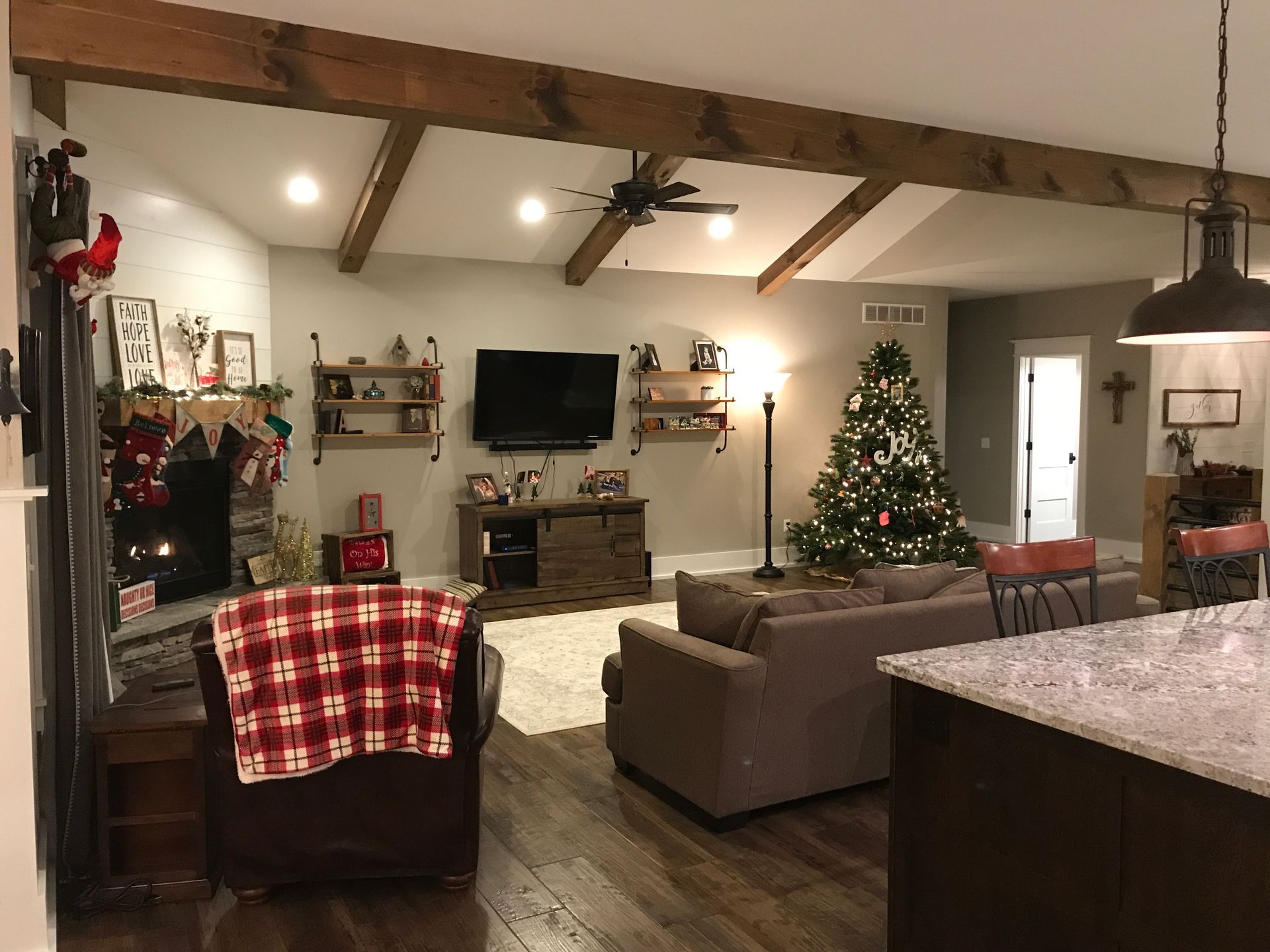 Cozy living room with Christmas tree, fireplace, TV, and plaid chairs beneath exposed beams