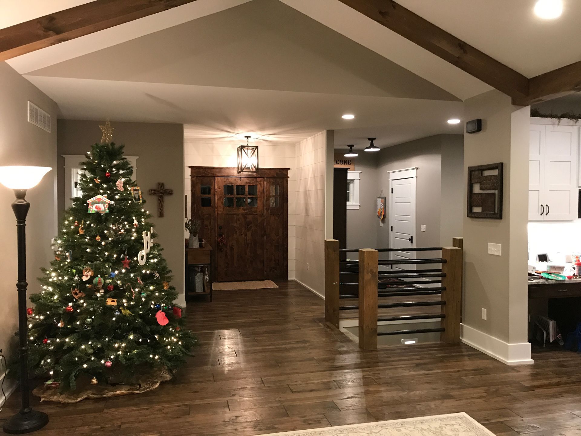 Warm living room with lit Christmas tree, wooden floors, exposed beams, and a staircase.