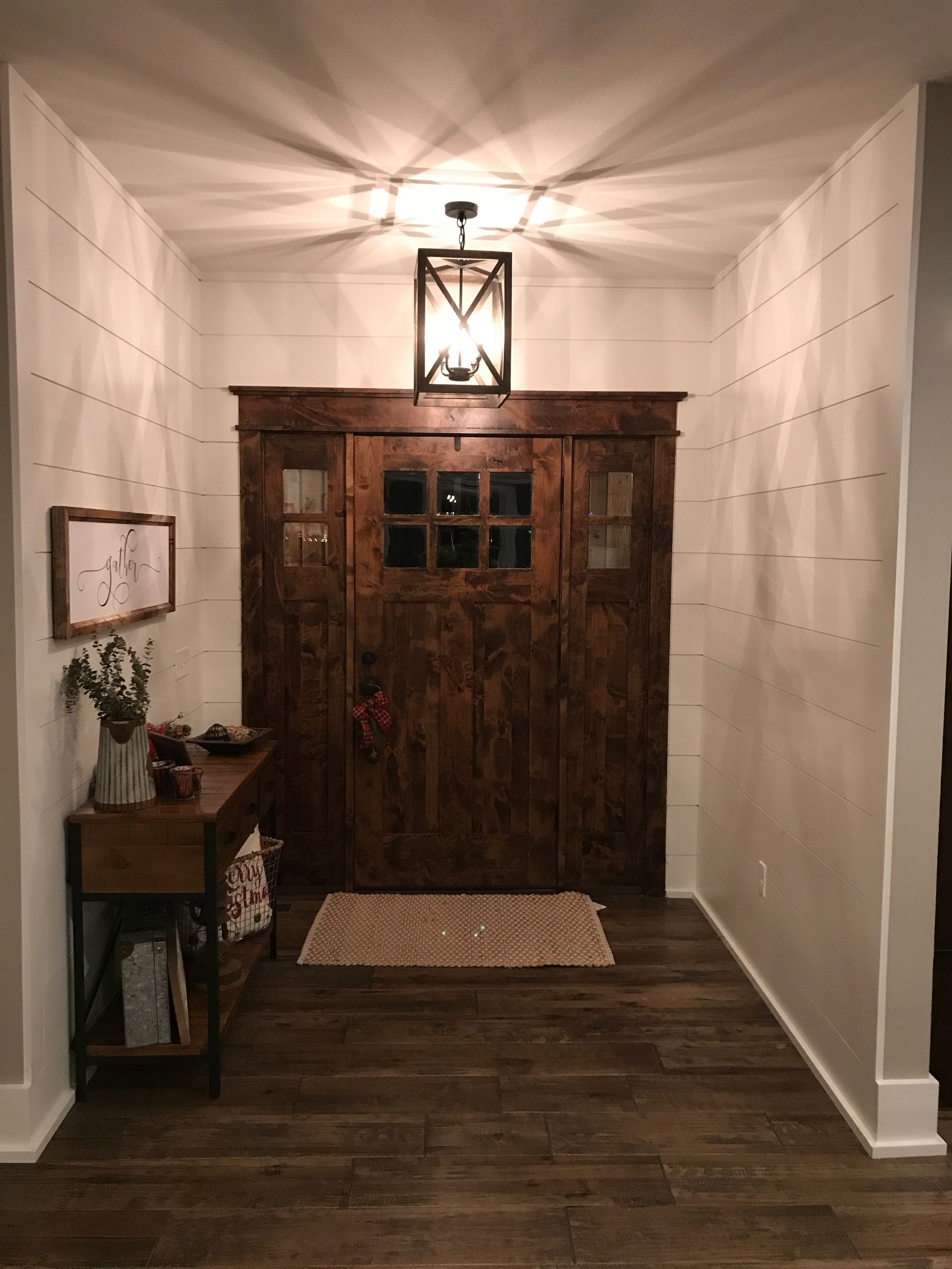 Narrow hallway with rustic wooden front door, white walls, ceiling light, and a small rug on dark wood floor