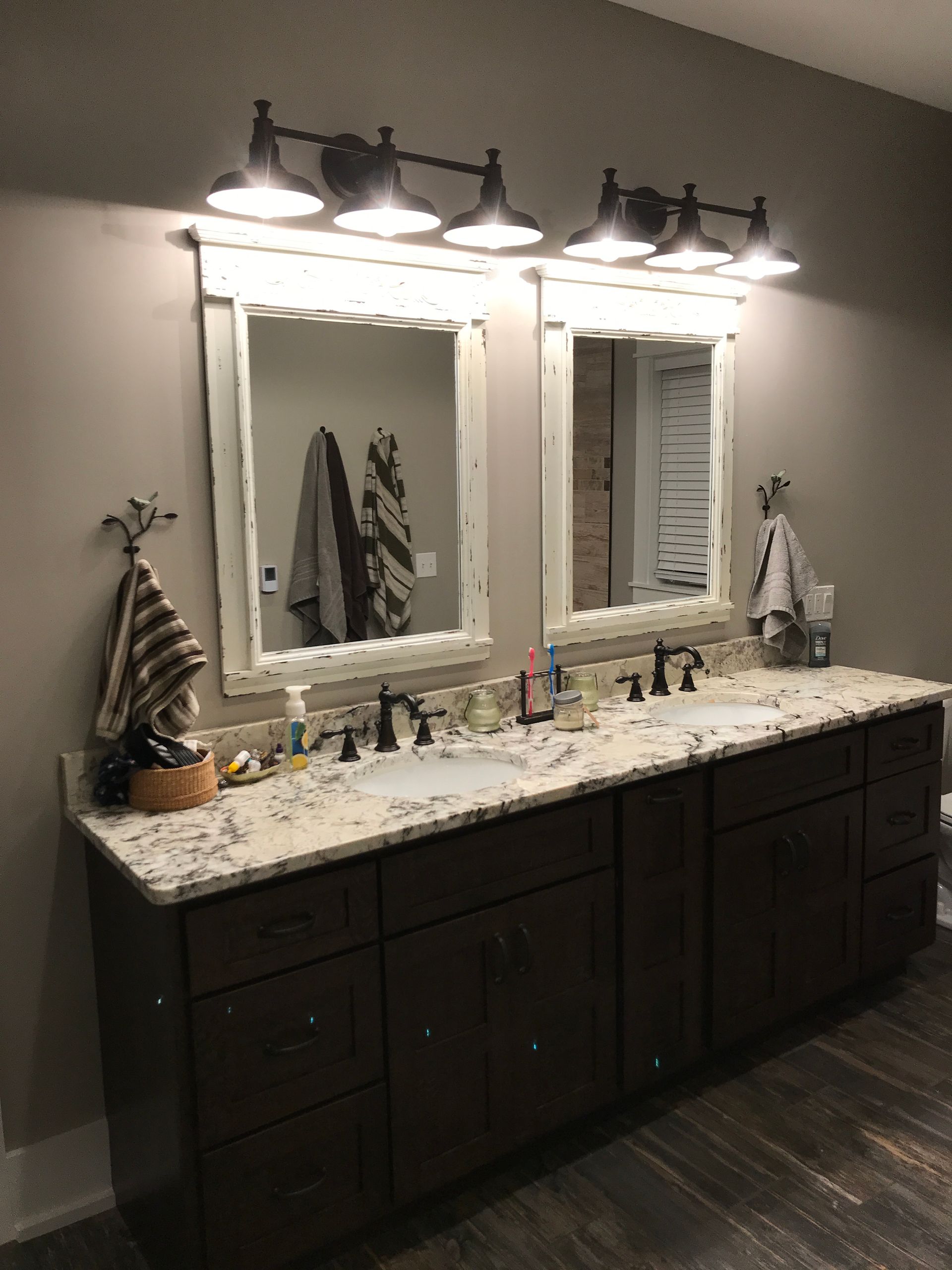 Modern bathroom vanity with double mirrors, granite countertop, and dark wood cabinets under bright lights.